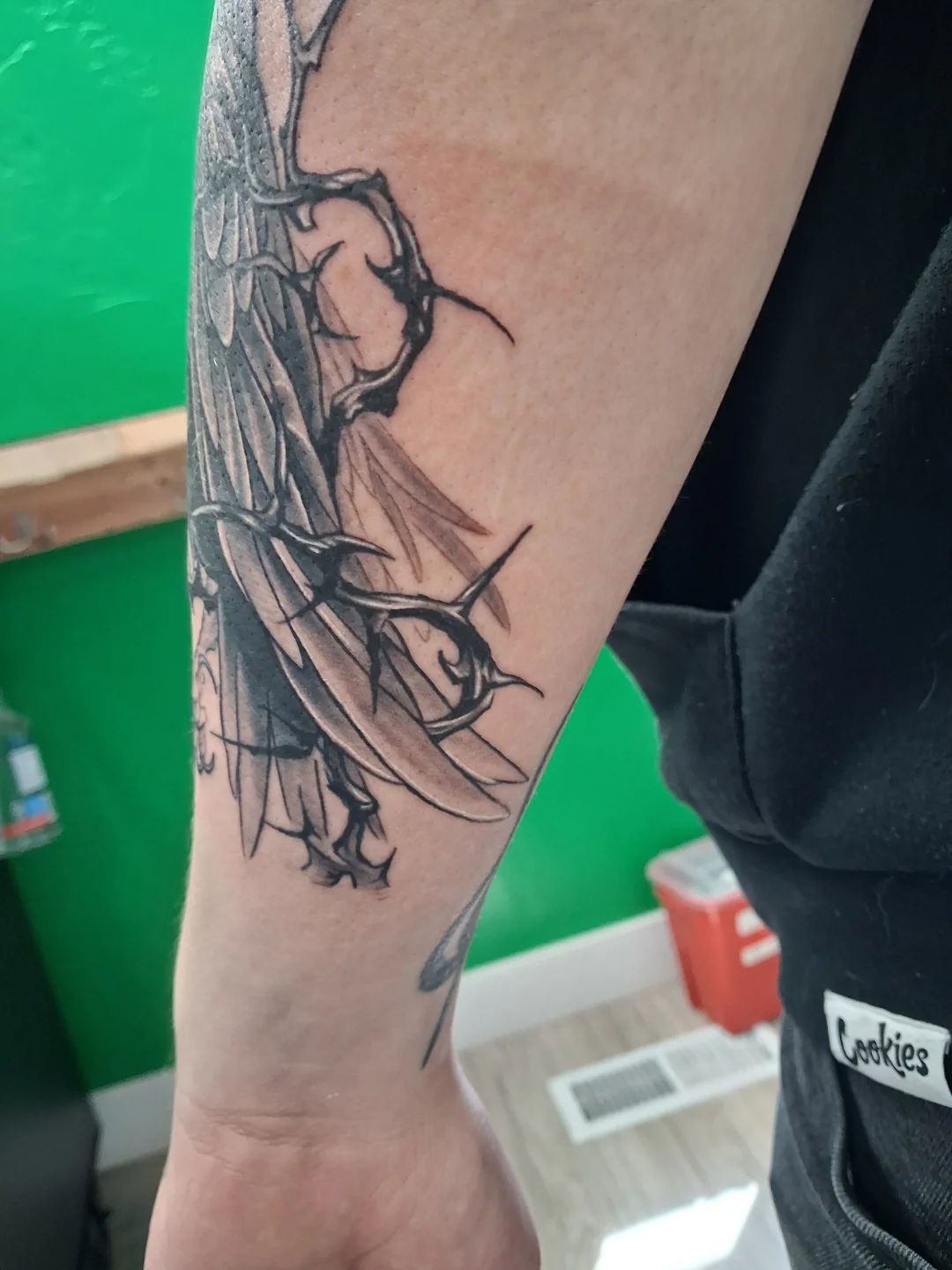 Wings and thorns black and grey tattoo on the forearm by James Ostler