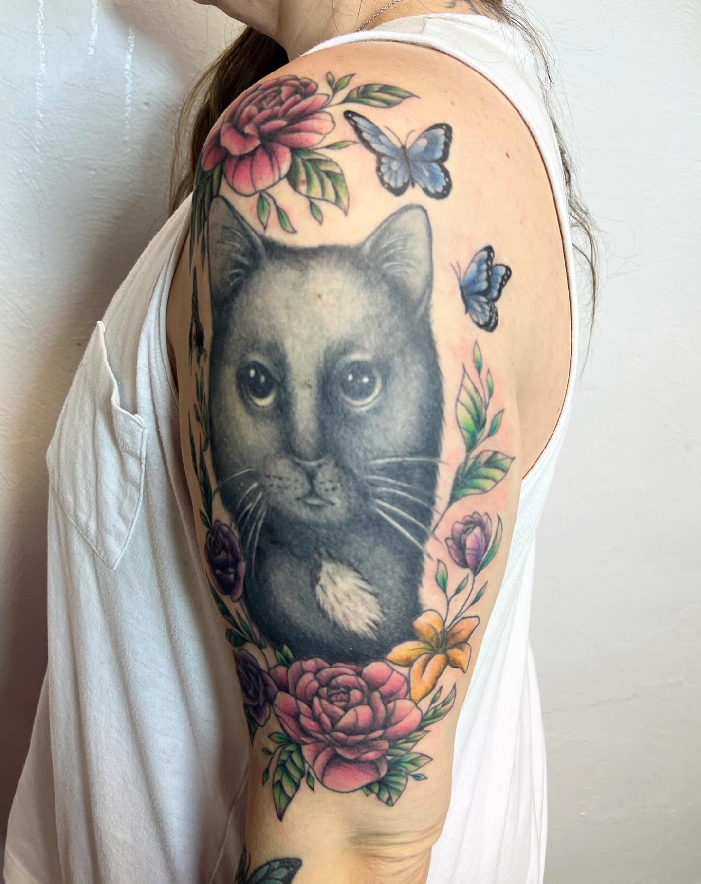 Cat with floral and butterfly details realism tattoo on the shoulder by Amber Rose