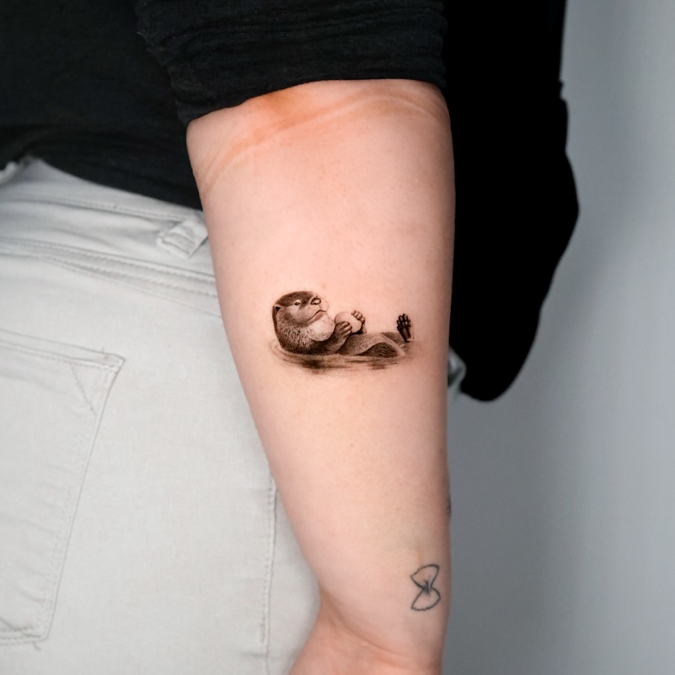 Otter holding a shell realism tattoo on the forearm by Fine Line, New York, New York