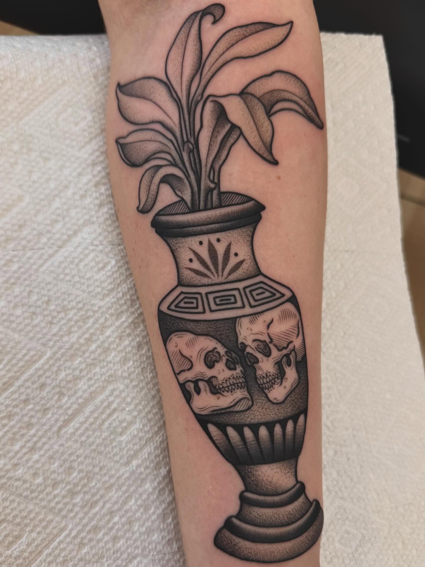 Urn with skulls and plant black and grey tattoo on the forearm by Stefany