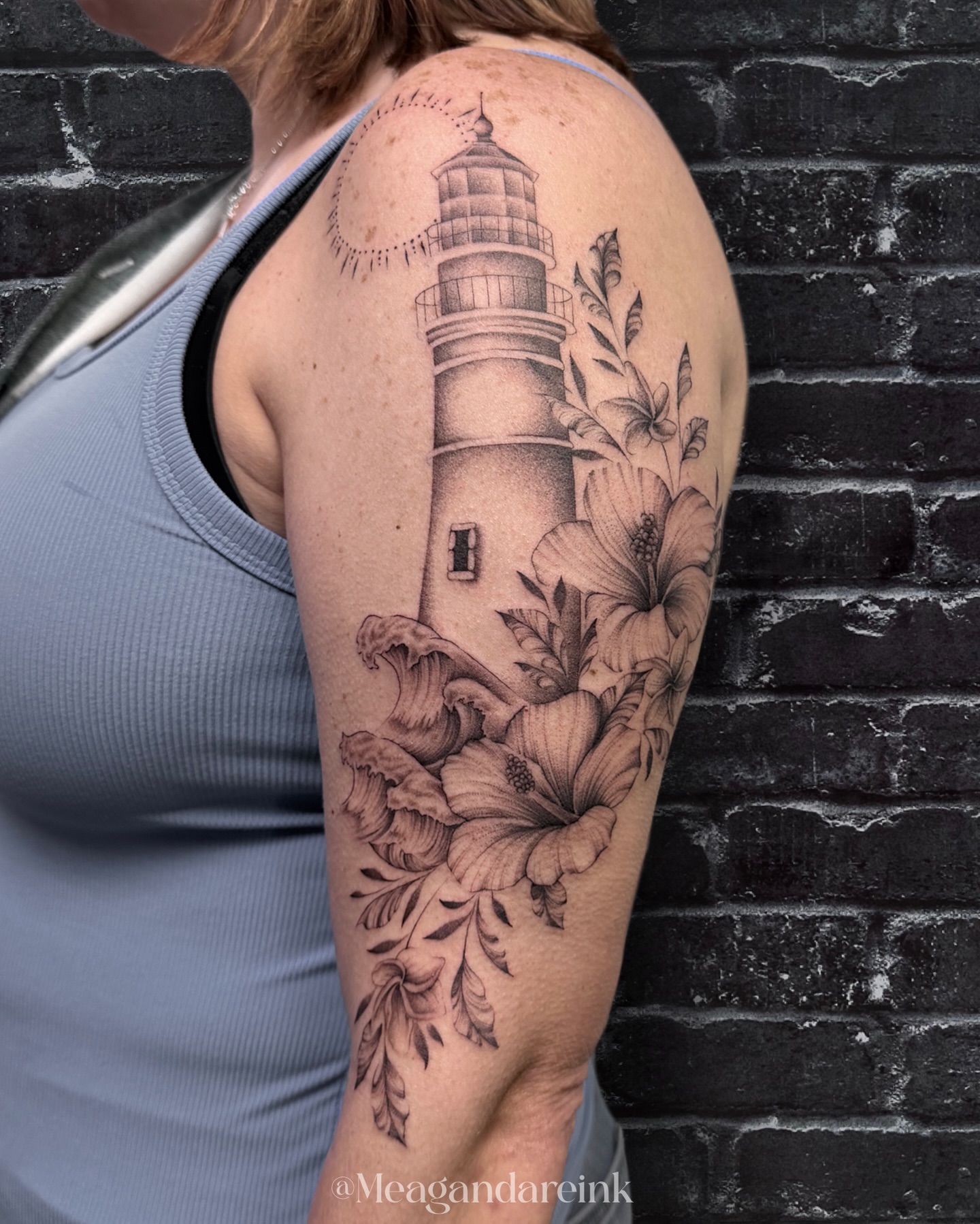 Lighthouse and flowers realism tattoo on the upper arm by Meagan Dare