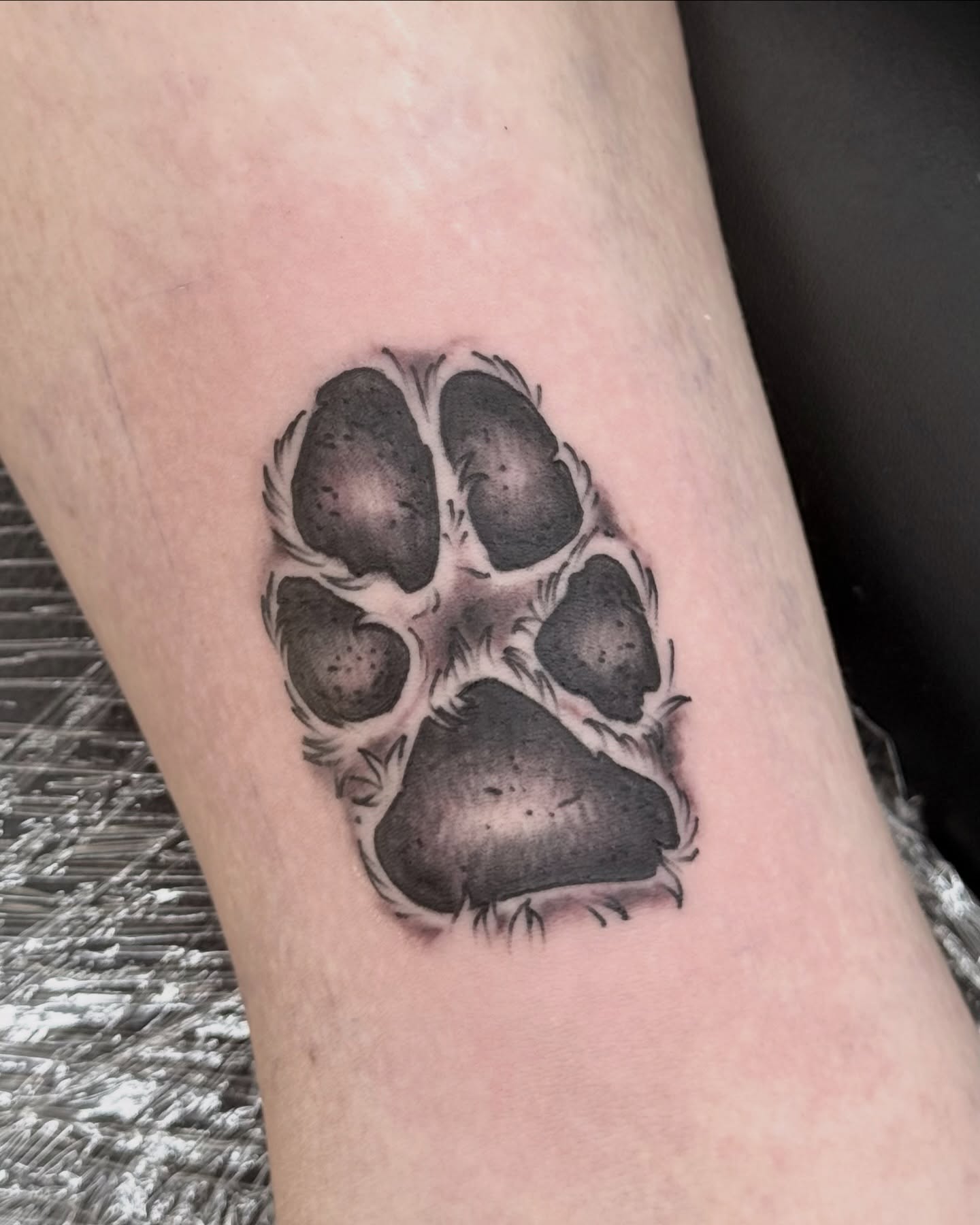Paw print black and grey tattoo on the forearm by autumn sky