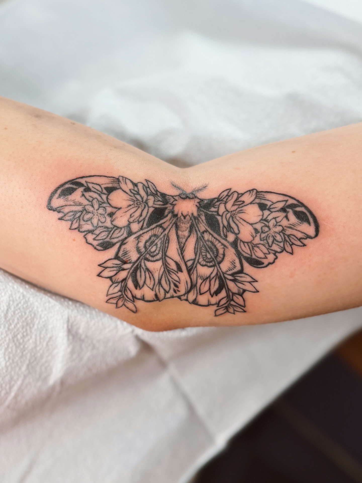 Moth with floral wings black and grey tattoo on the forearm by Emma Berger