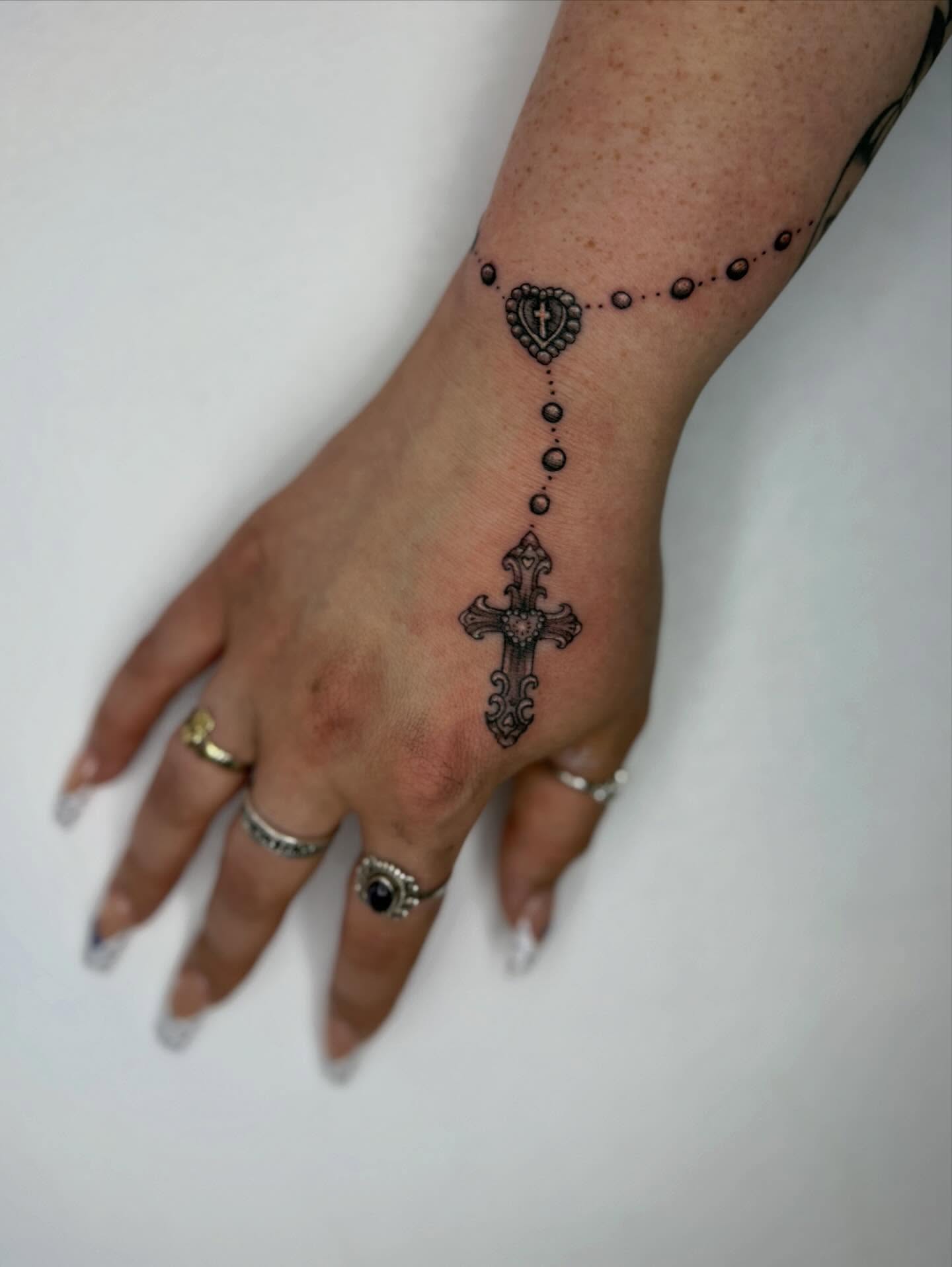 Cross and rosary black and grey tattoo on the hand by Sasha “Sashimi” Shabasov