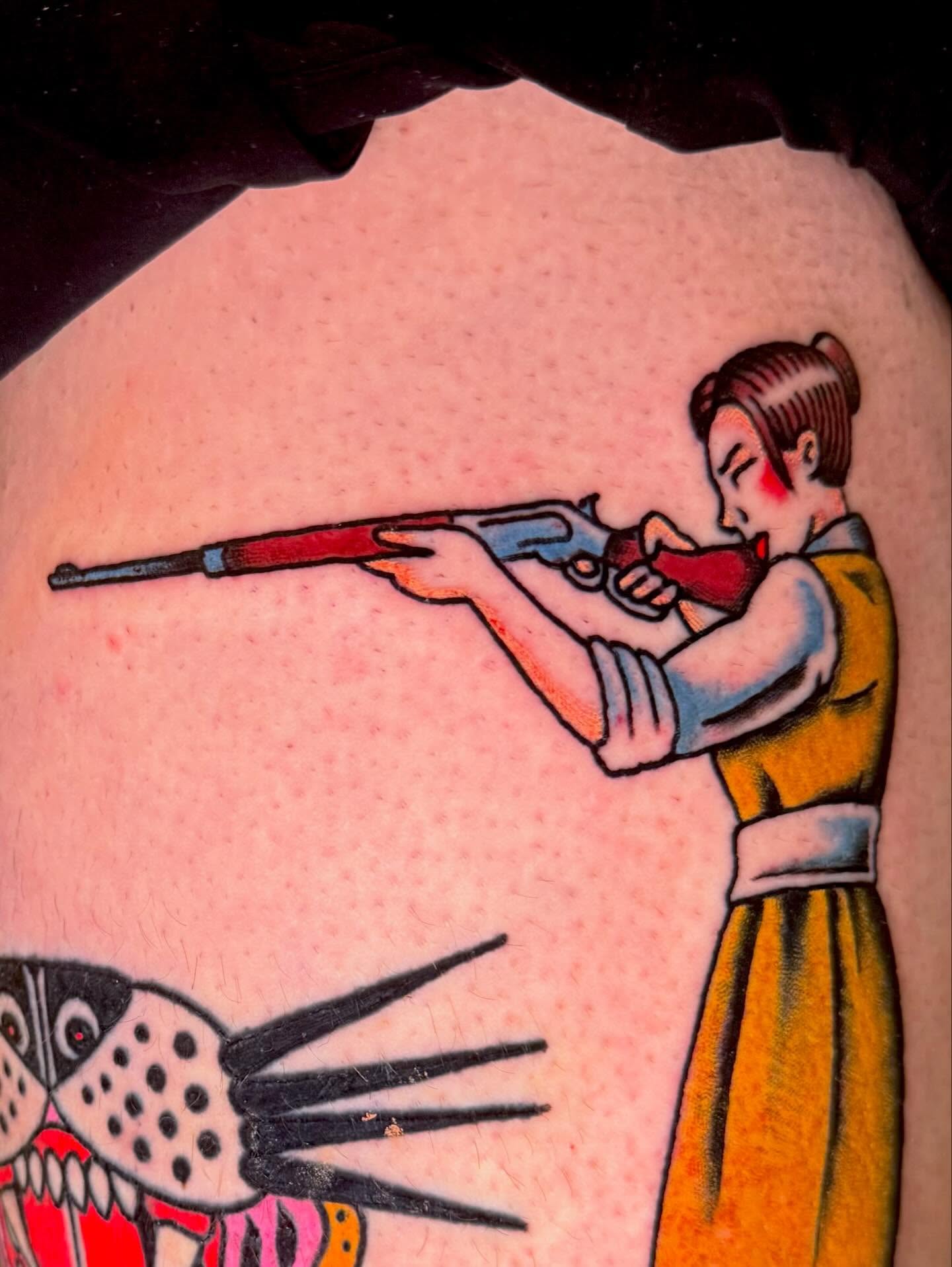 Woman with shotgun American traditional tattoo on the thigh by Henry Bubula, Minneapolis, Minnesota