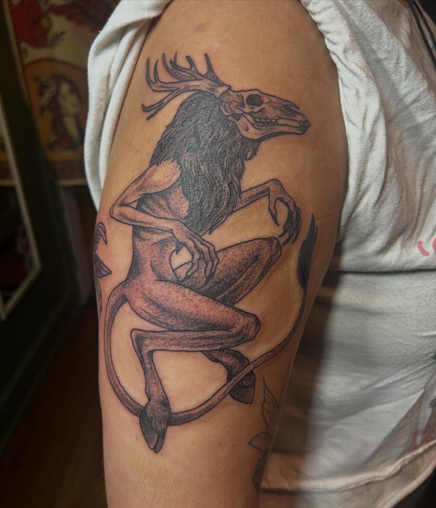Creature with deer skull head dark art tattoo on the upper arm by Jaime Gaiti
