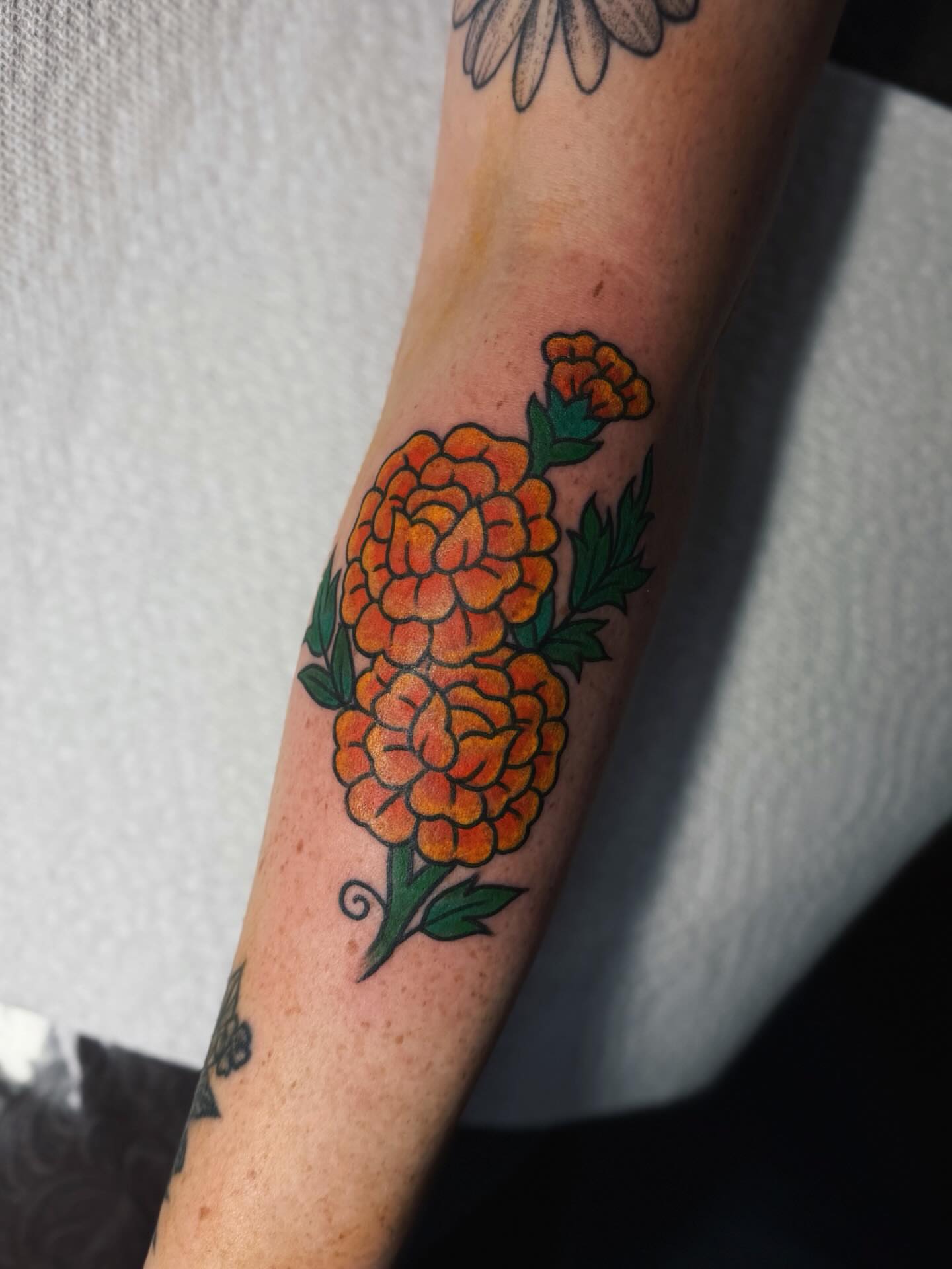 Marigold flowers American traditional tattoo on the forearm by @amandahowtattoo