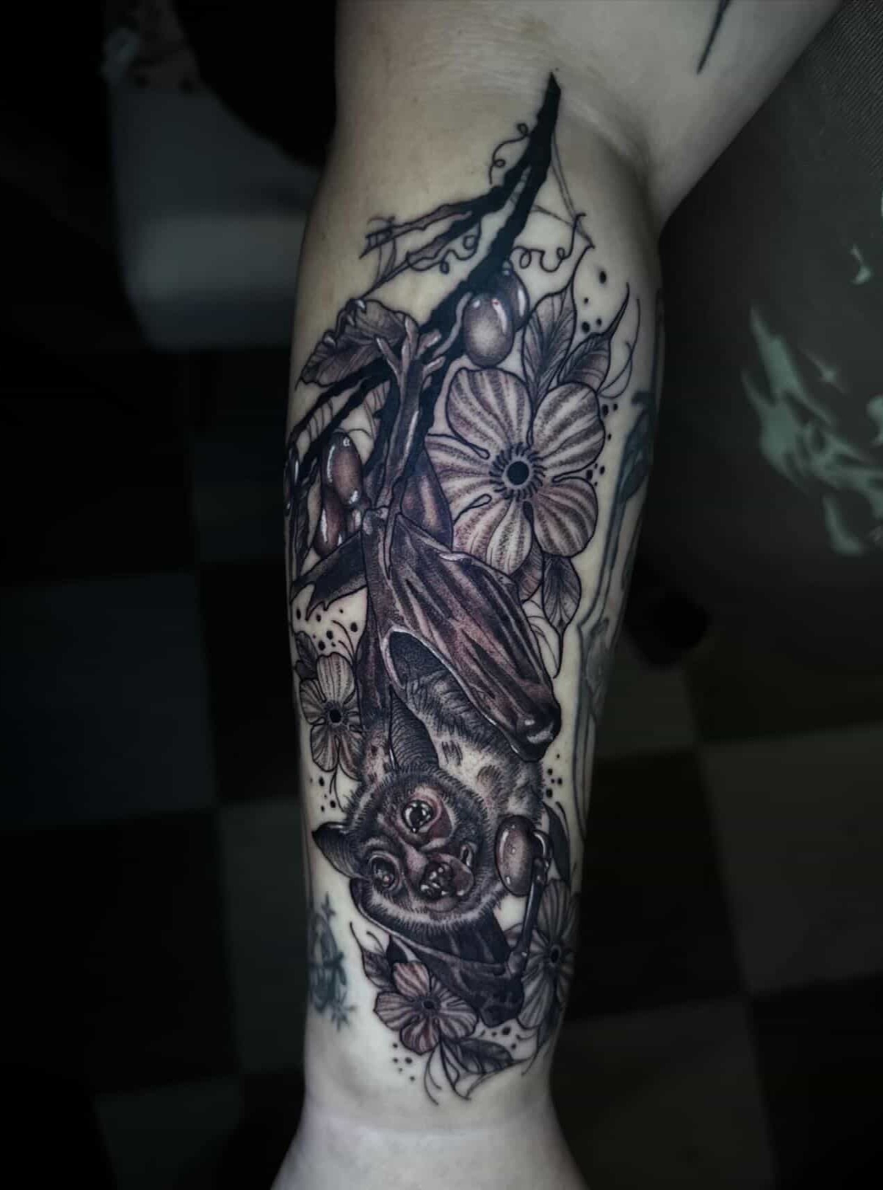 Bat and flowers realism tattoo on the forearm by Sierra