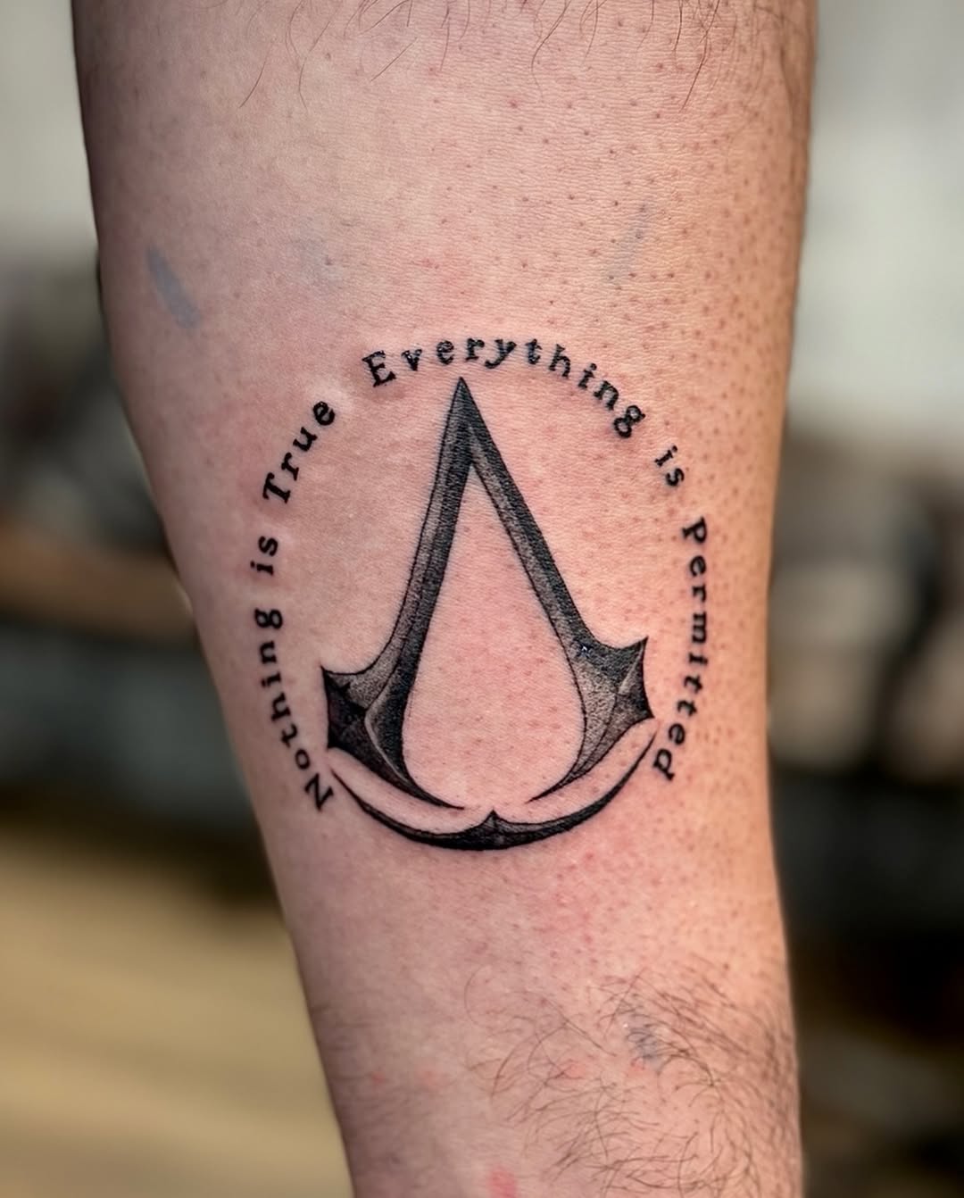 Assassin's Creed logo with lettering tattoo on the forearm by David