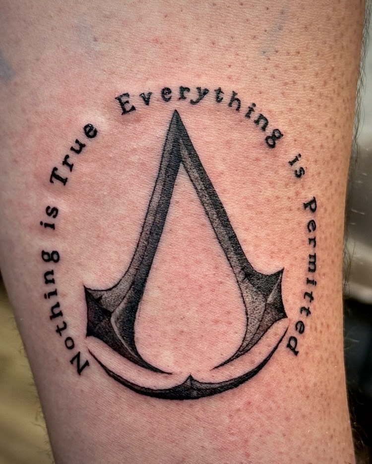 Assassin's Creed logo with text tattoo on the forearm by David