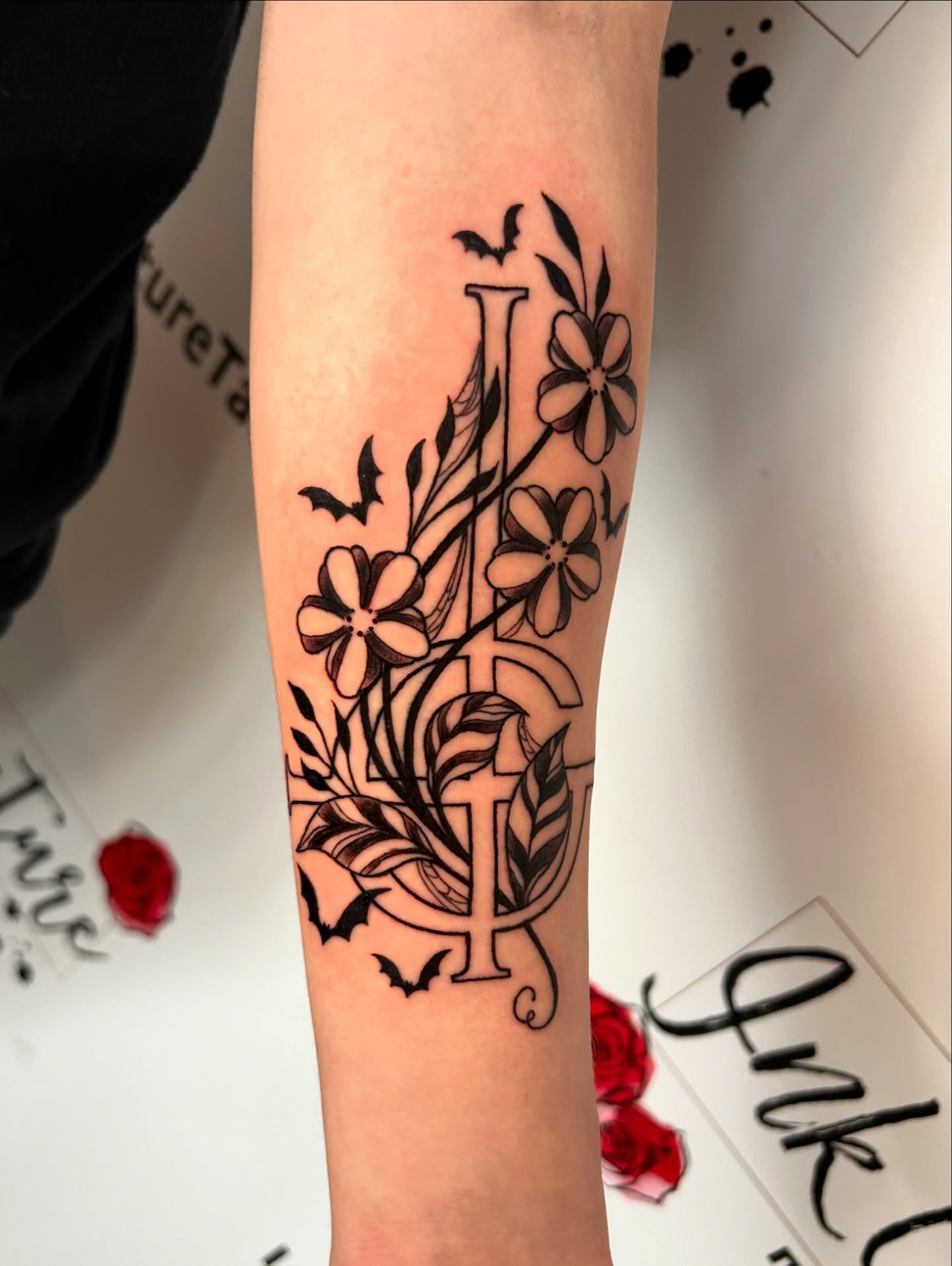 Floral and bat design black and grey tattoo on the forearm by Tess