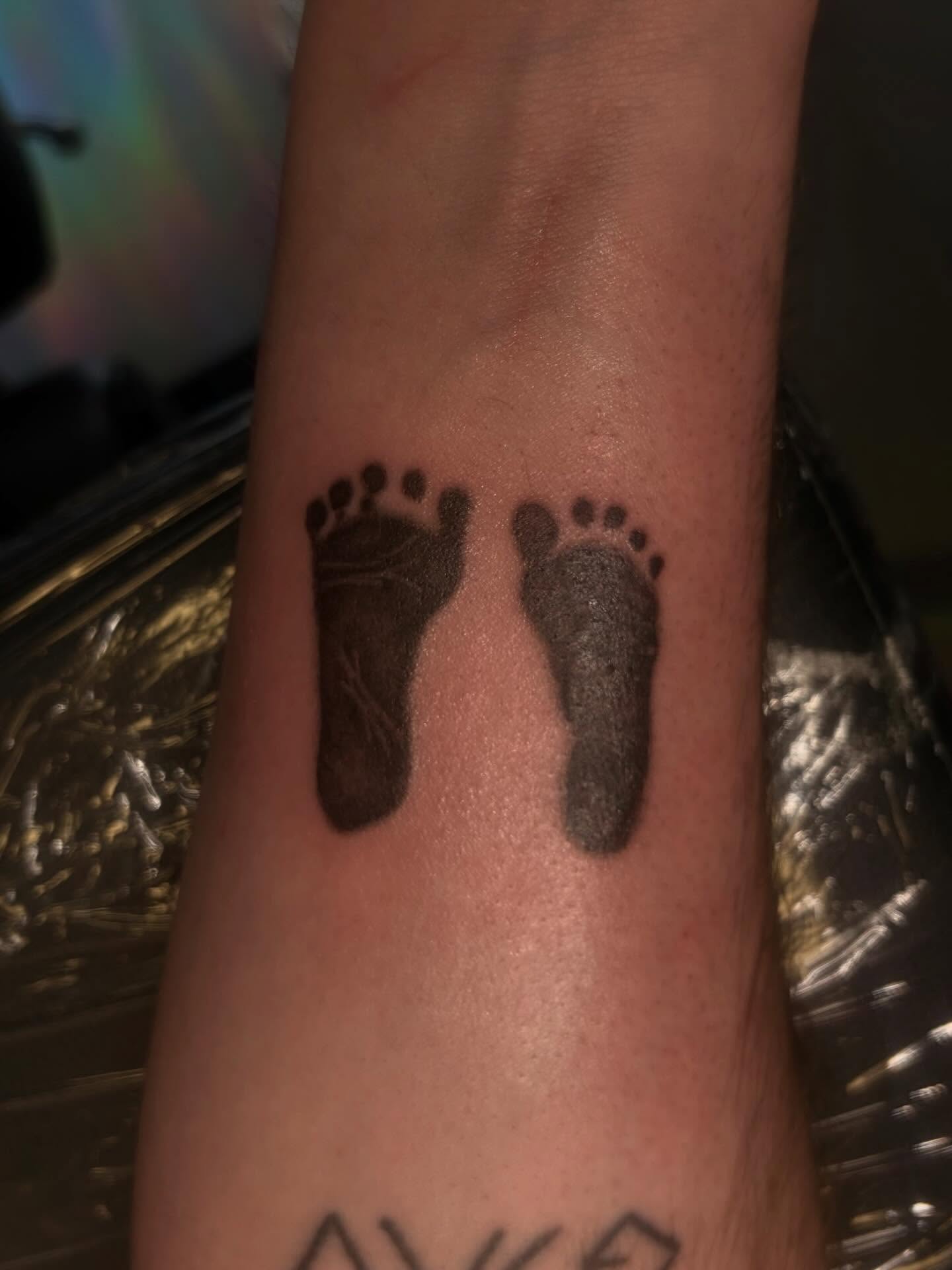 Footprints black and grey tattoo on the forearm by Melissa