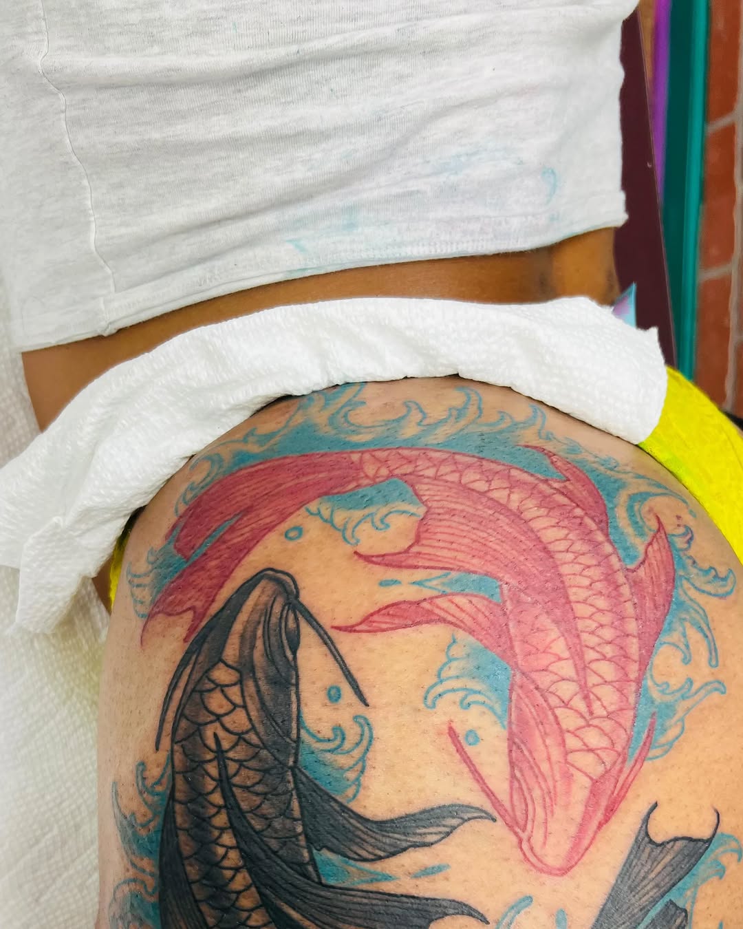 Koi fish and waves tattoo on the thigh by Watson Gutkowski