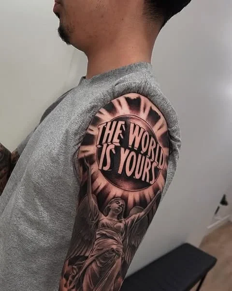 Statue with wings realism tattoo on the upper arm by Magdalena Davis