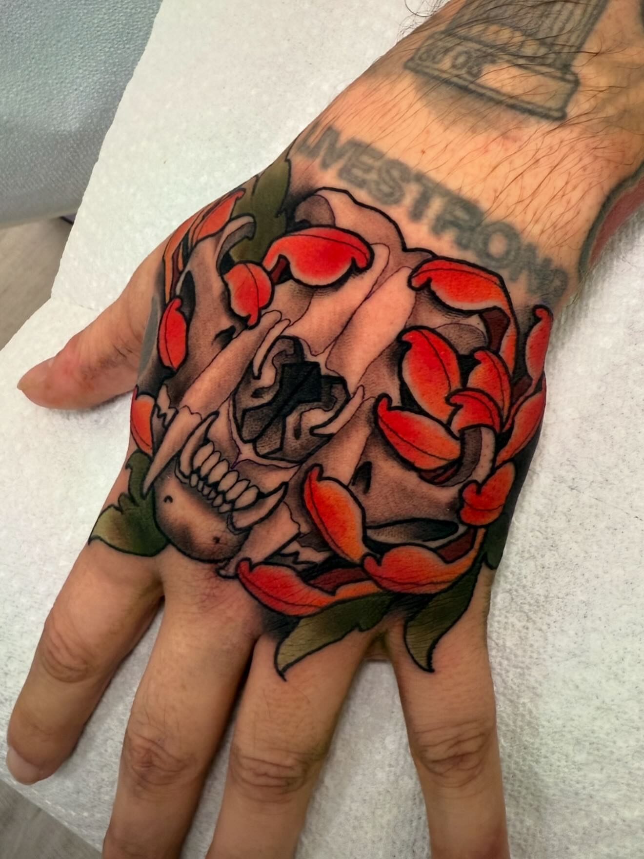 Skull and flowers American traditional tattoo on the hand by Kyle Behr