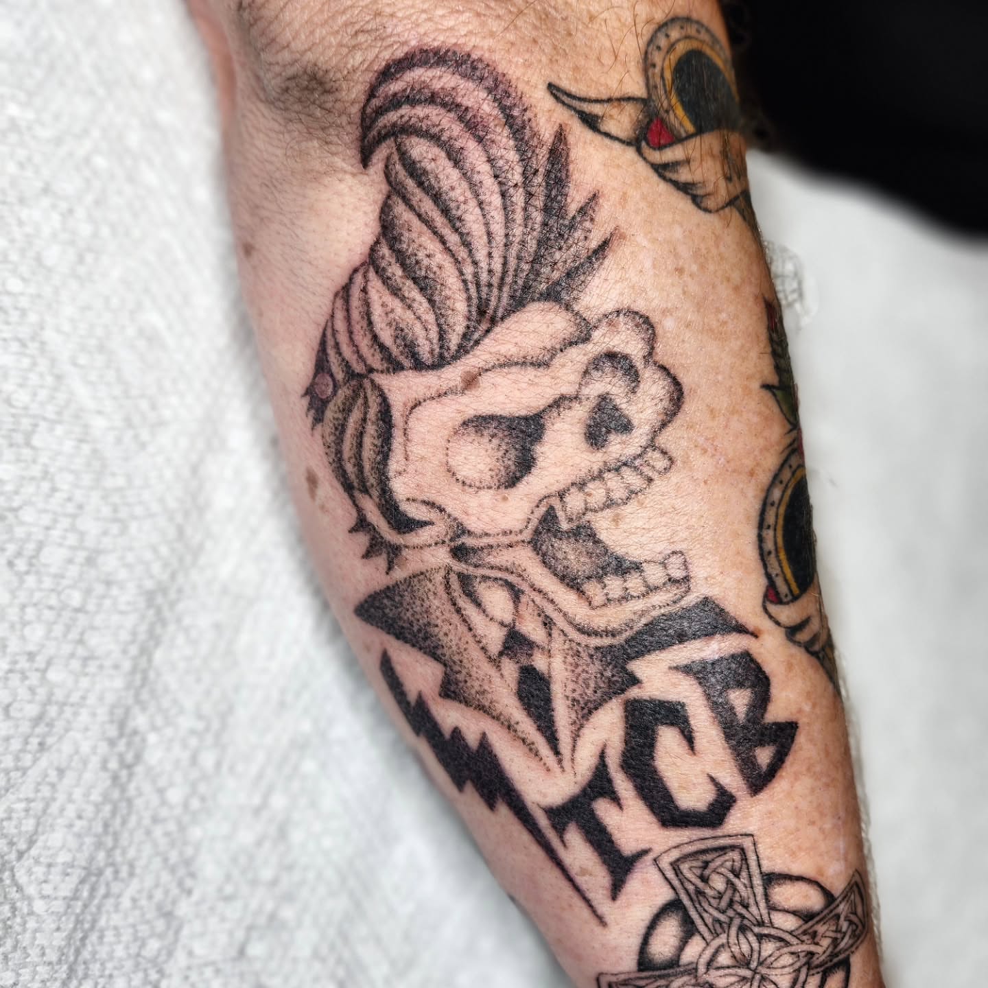 Skull with Mohawk black and grey tattoo on the forearm by Kelly Zito