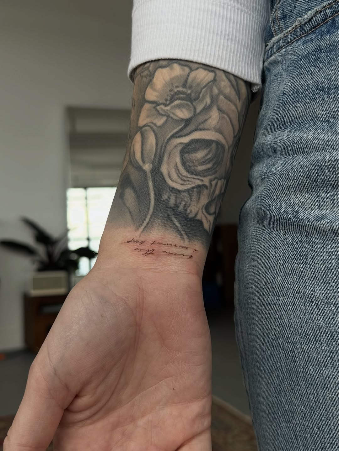 Skull and flowers with script lettering tattoo on the forearm by @taravychi