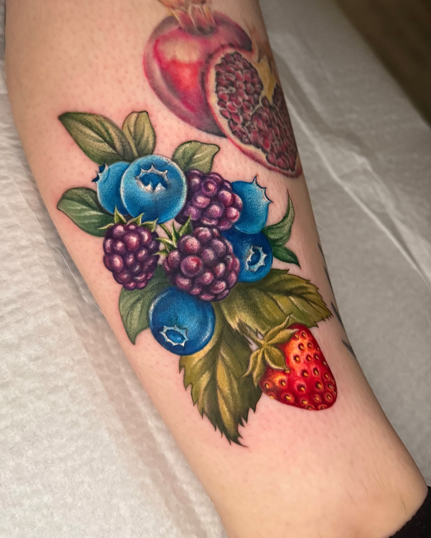 Berries and pomegranate realism tattoo on the forearm by Nichole Lorence