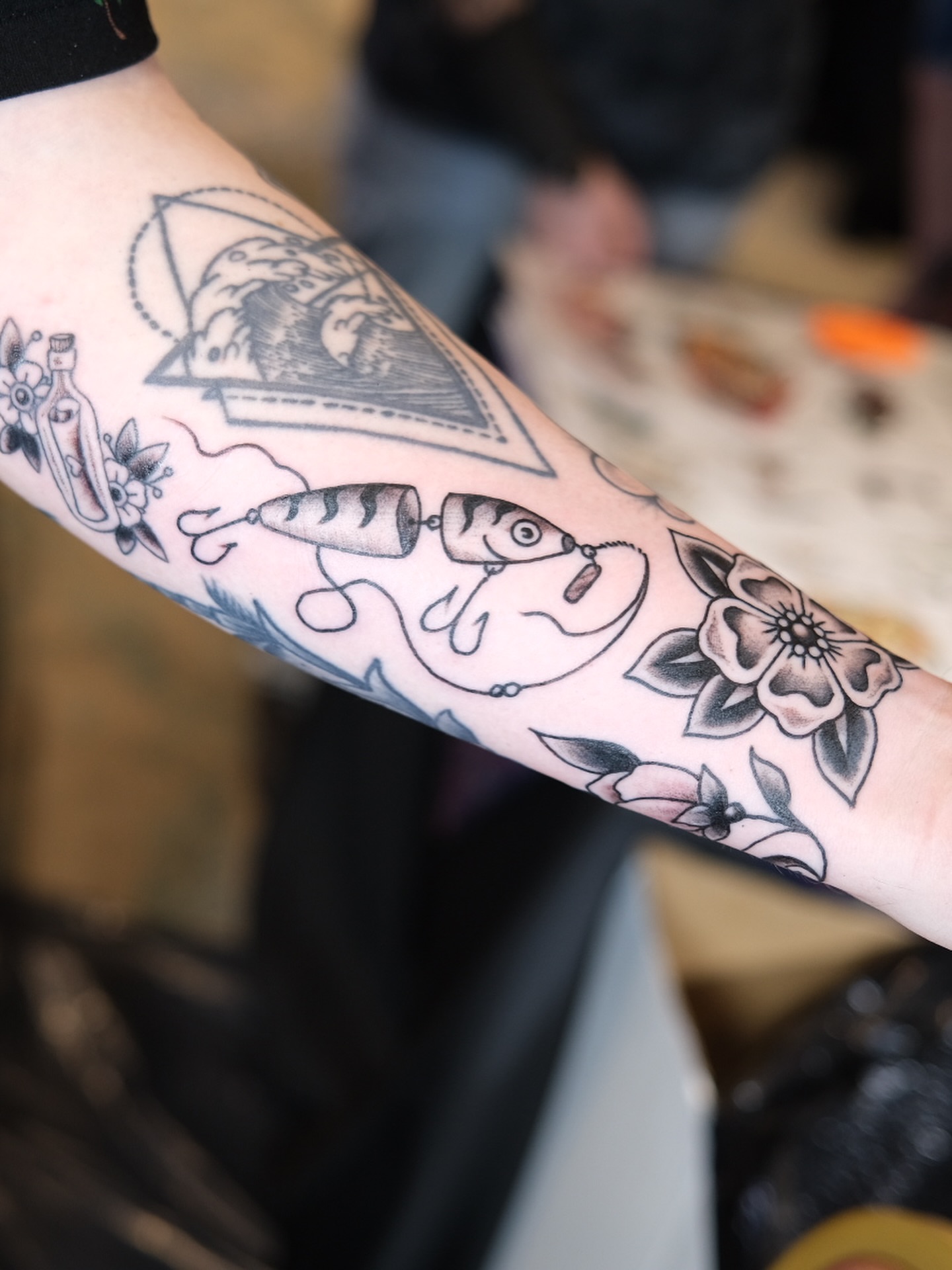 Fishing lures and flowers black and grey tattoo on the forearm by Zak Colburn
