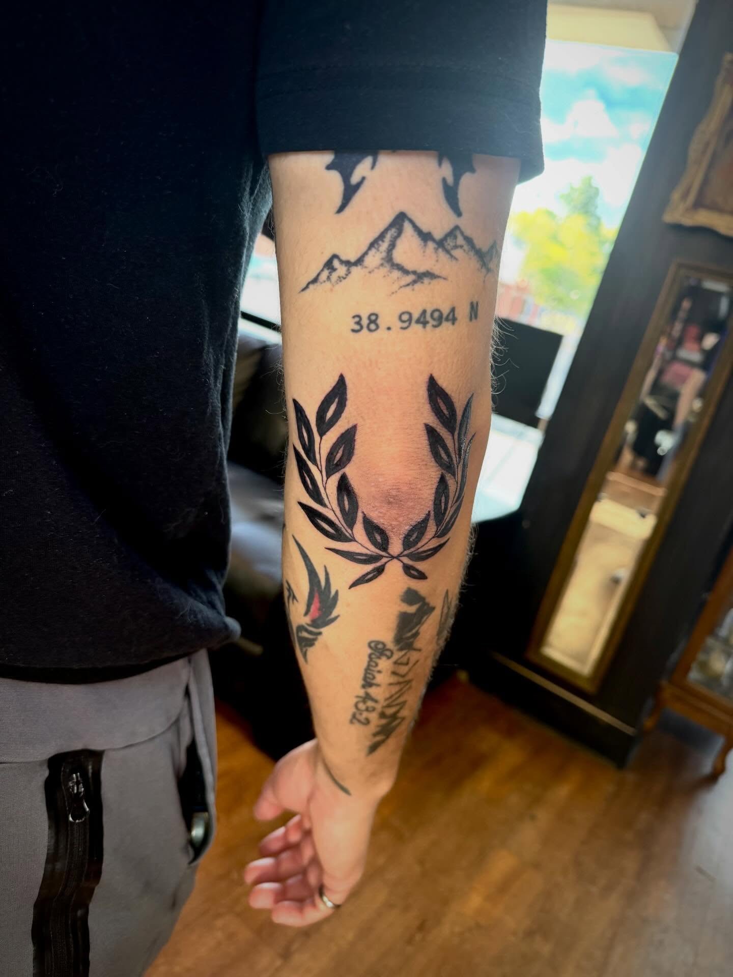 Mountains and laurel wreath black and grey tattoo on the forearm by Mikey