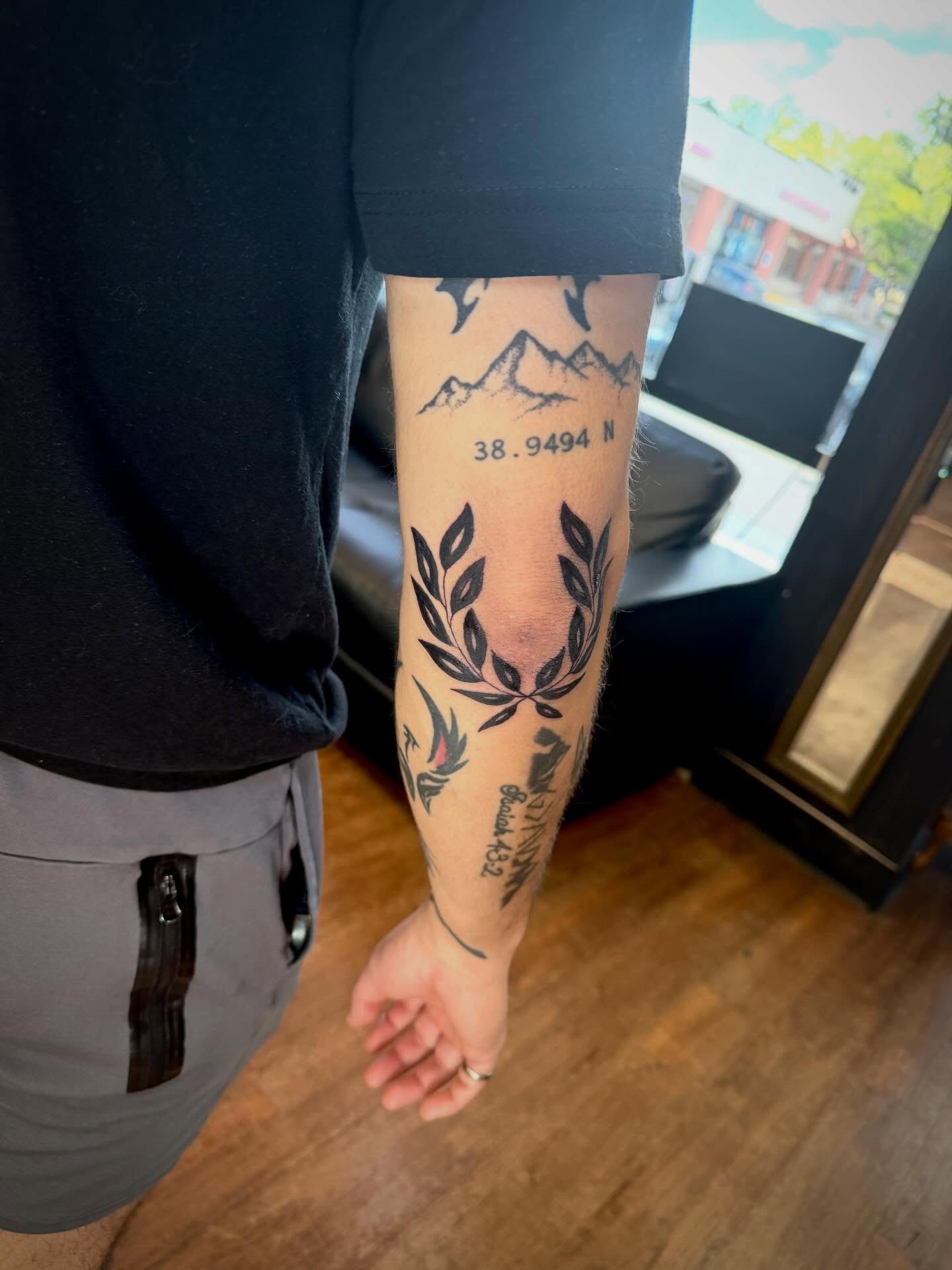 Mountains and laurel wreath black and grey tattoo on the forearm by Mikey