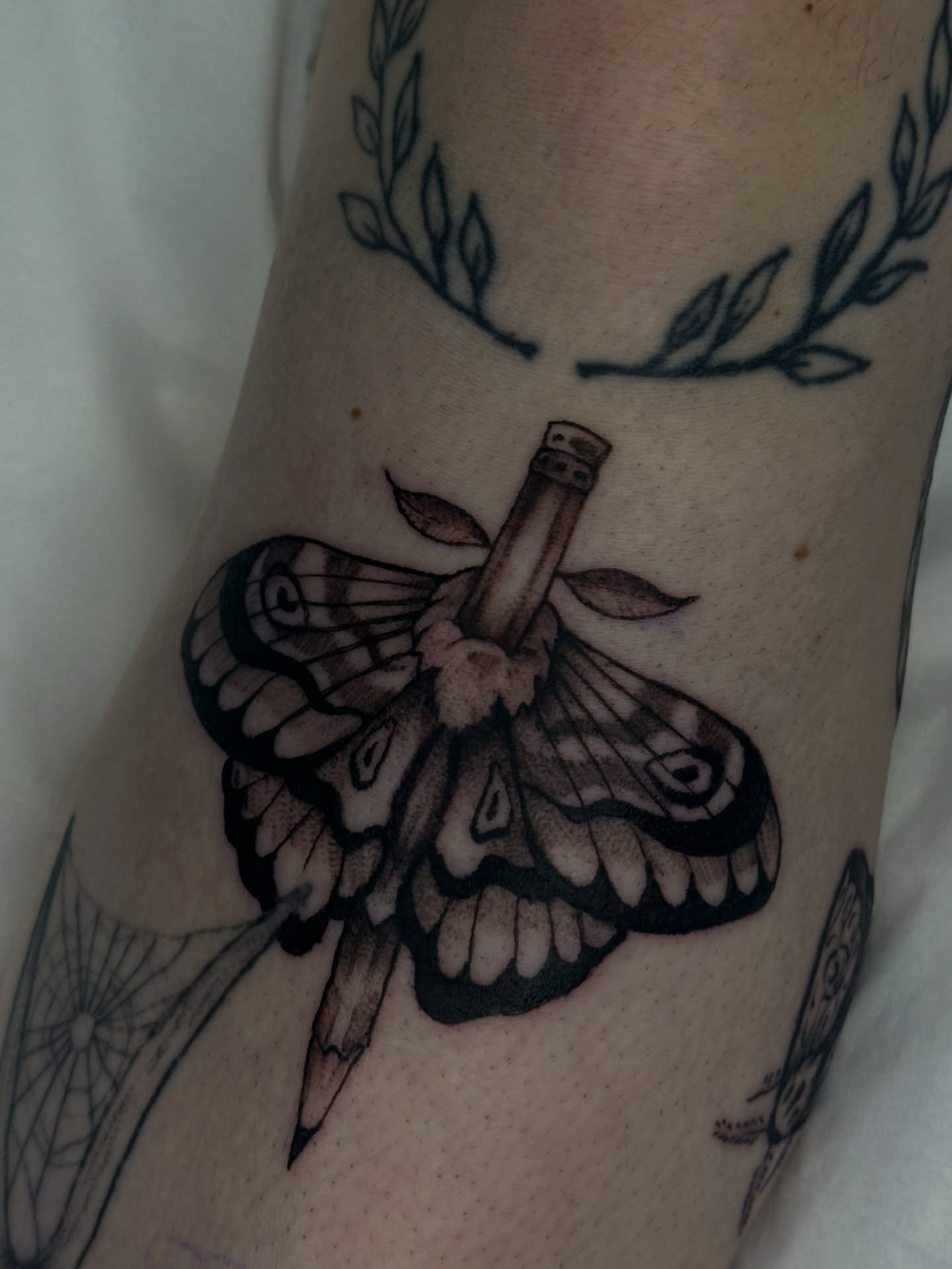 Moth and bottle black and grey tattoo on the forearm by Halle Cooper