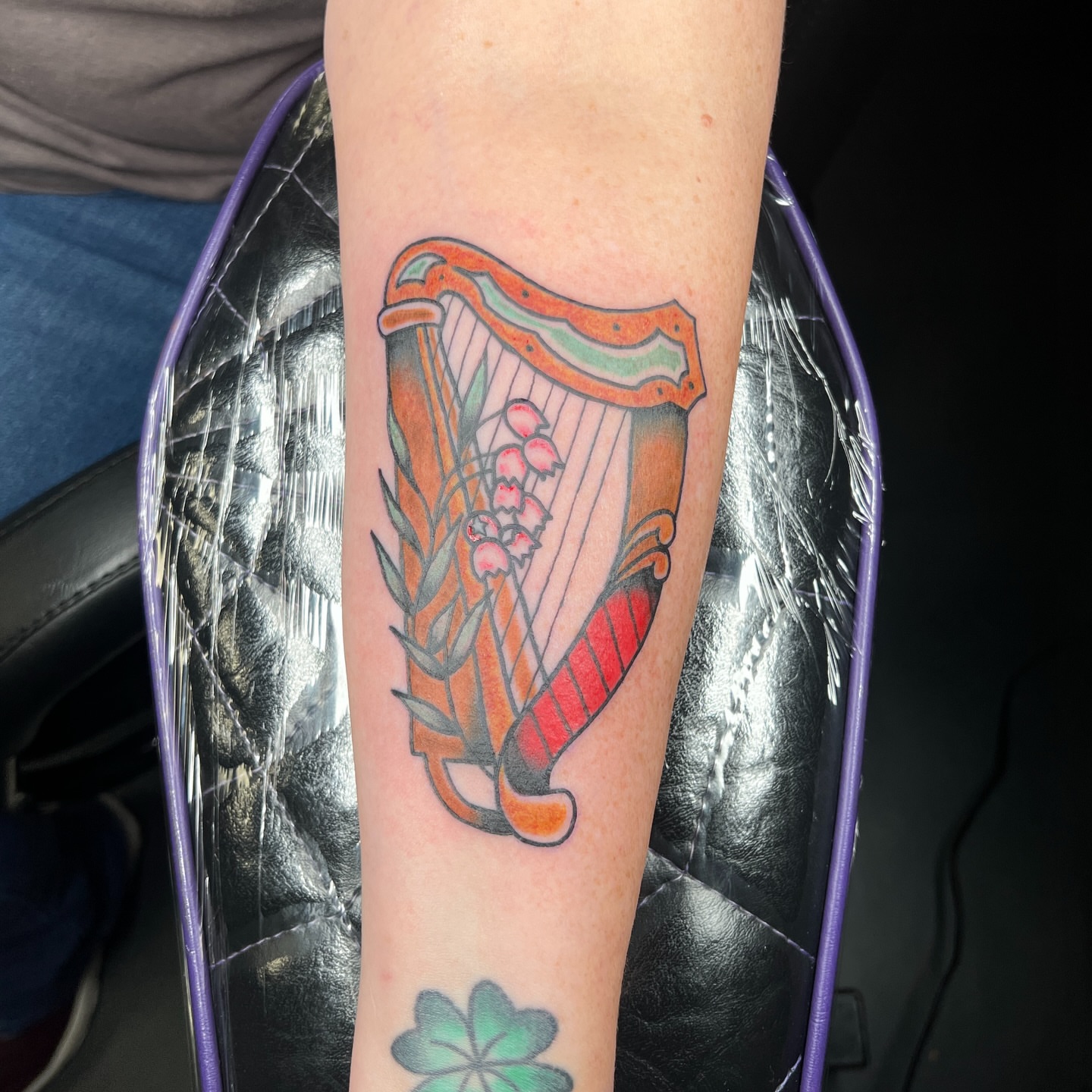 Harp and lilies of the valley American traditional tattoo on the forearm by Brian Mock