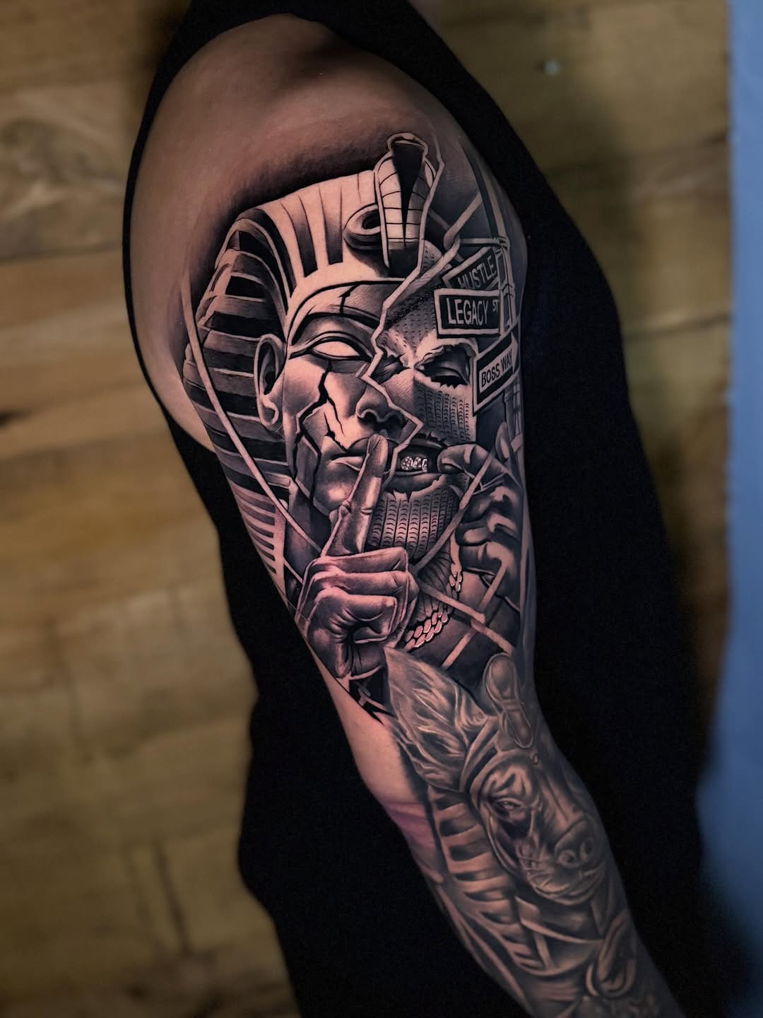 Pharaoh and Anubis with street signs surrealism tattoo on the upper arm by Miles Johnson