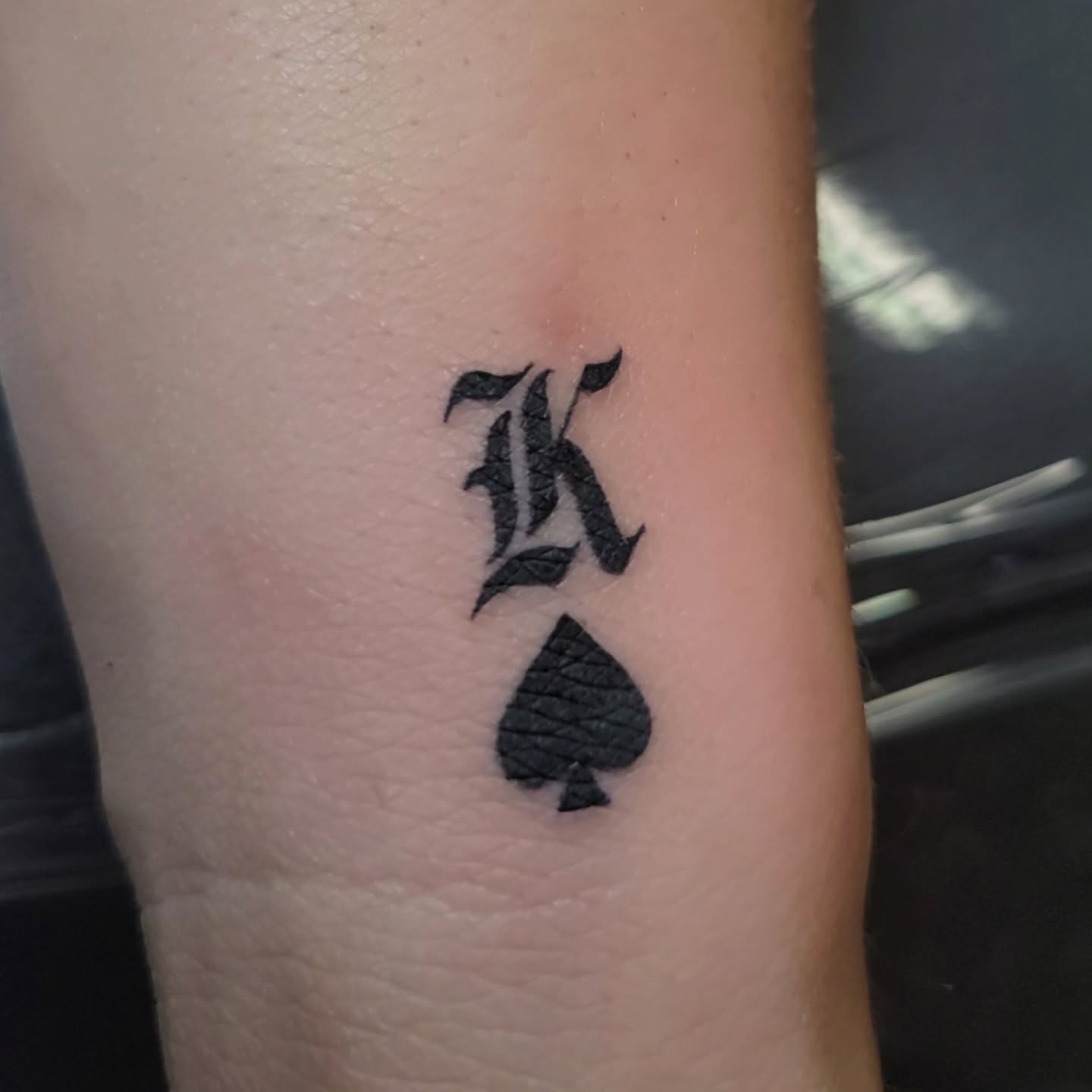 Spade and letter K black and grey tattoo on the forearm by Marina Cobb