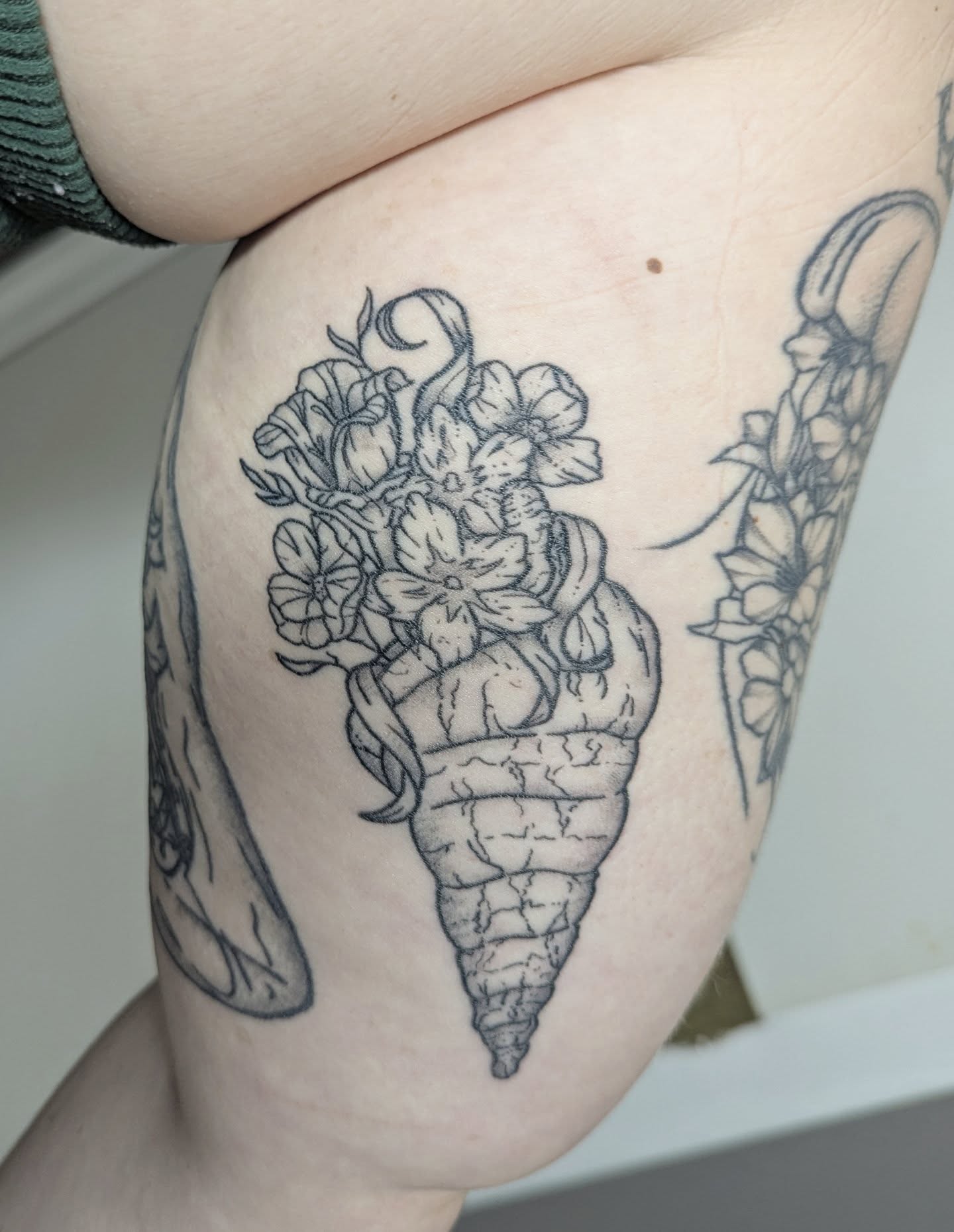 Flower bouquet in shell black and grey tattoo on the thigh by Patricio