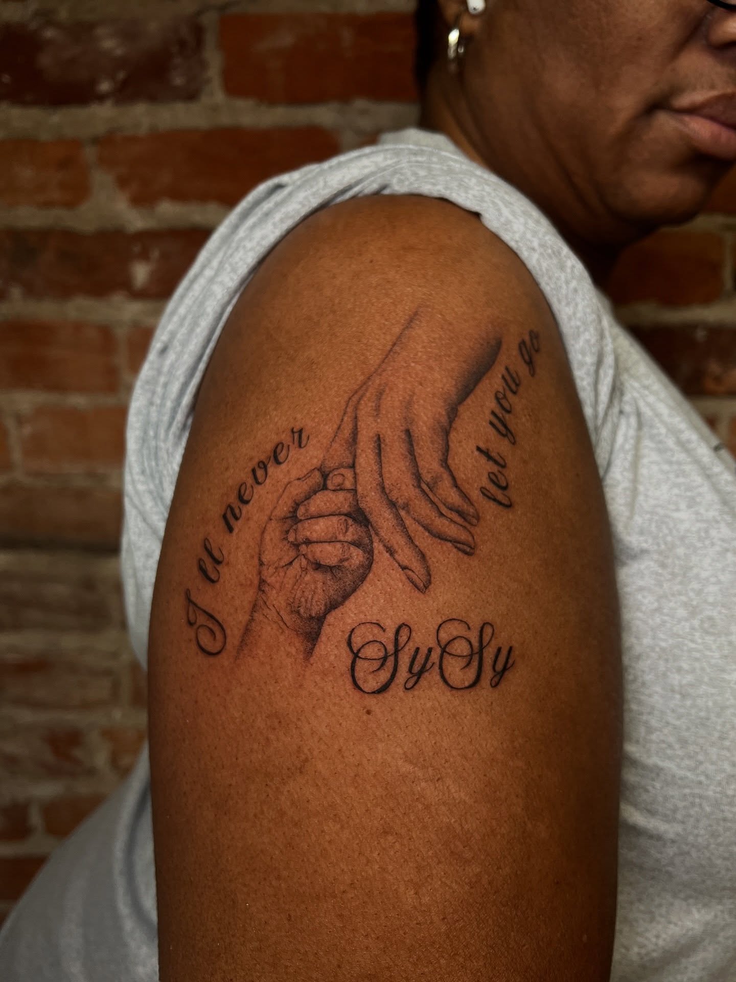 Holding hands black and grey tattoo on the shoulder by Uncomfy Comfort Tattoos LLC