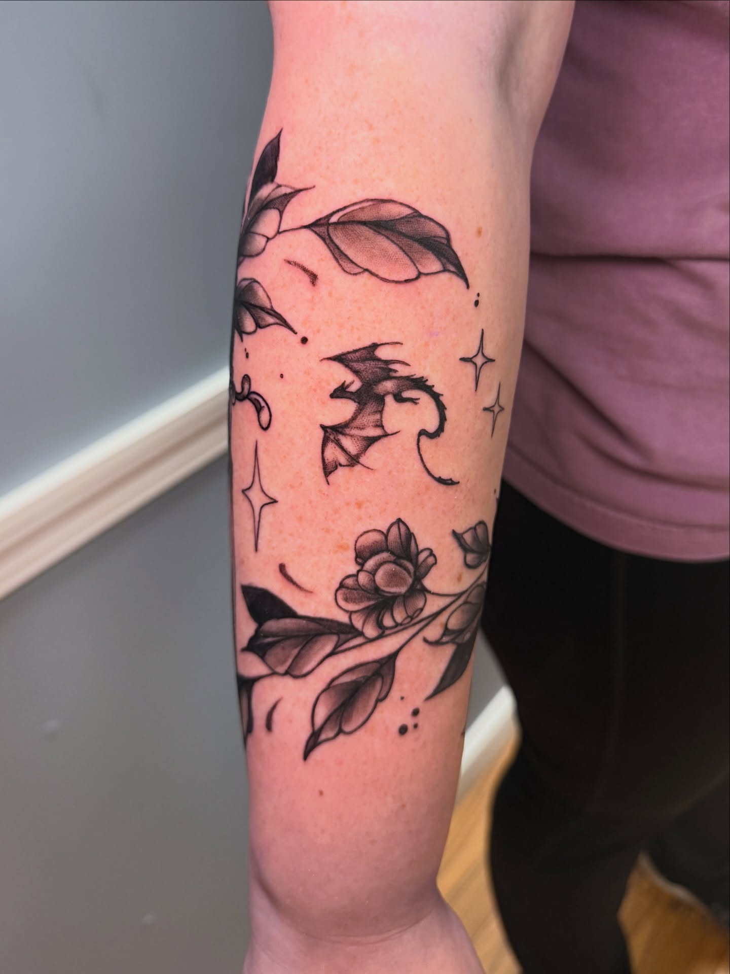 Bat and flowers black and grey tattoo on the forearm by Breanna Fraielli