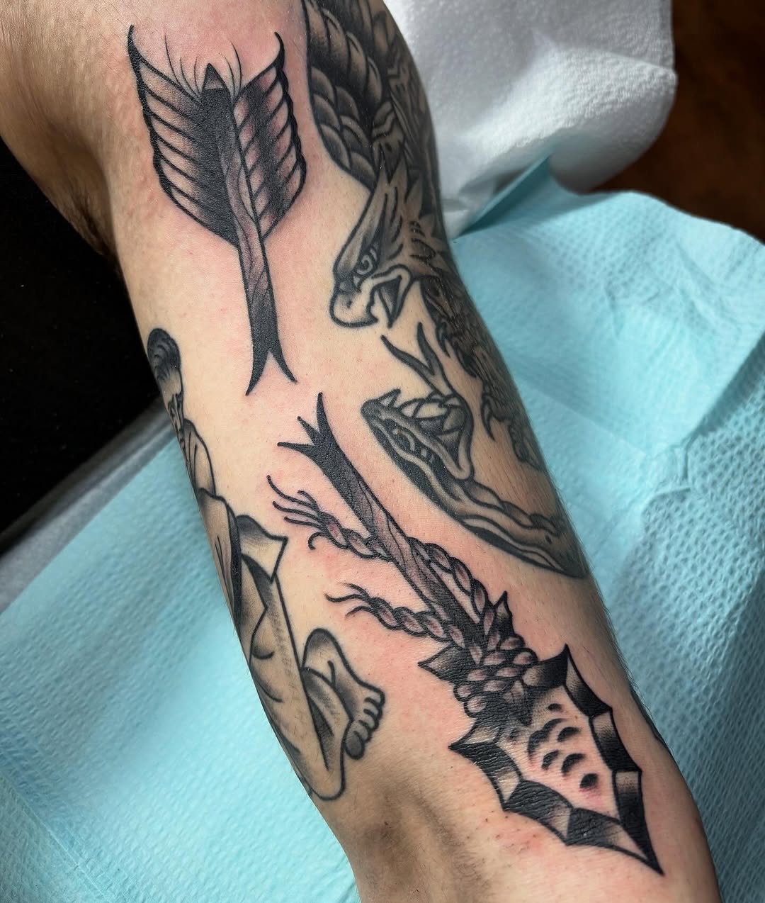 Arrow, eagle, snake, figure ignorant tattoo on the forearm by Tom Wenzell
