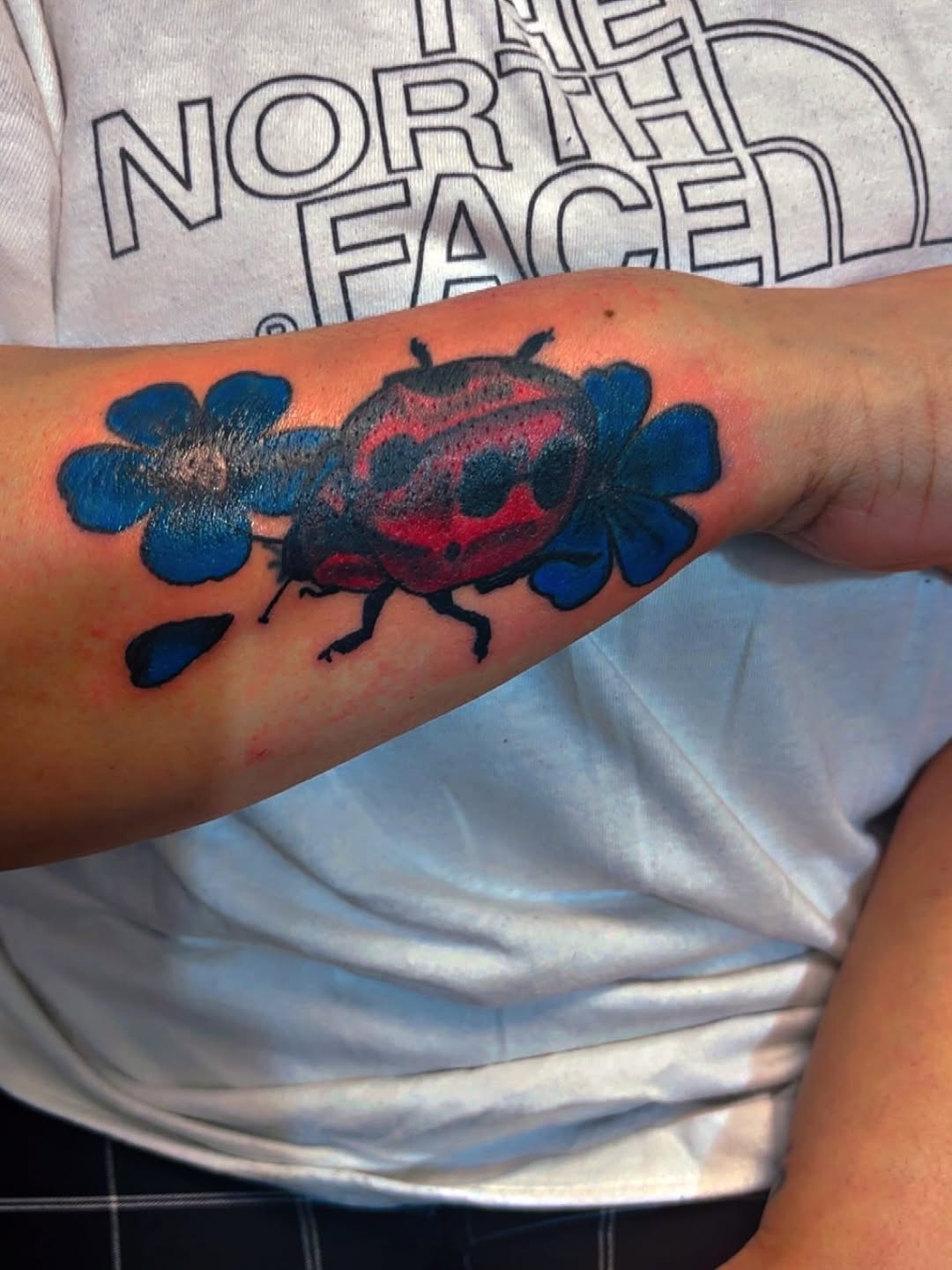Ladybug and flowers tattoo on the forearm by Syneca Wilson, Acton, Massachusetts