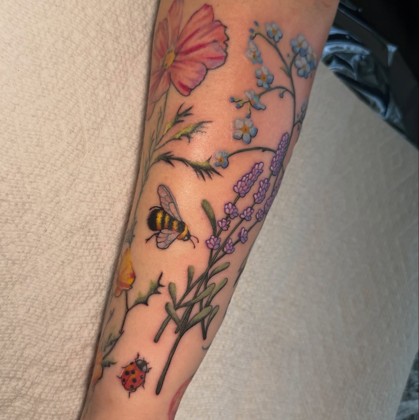 Floral and bee realism tattoo on the forearm by Lyndze Masters
