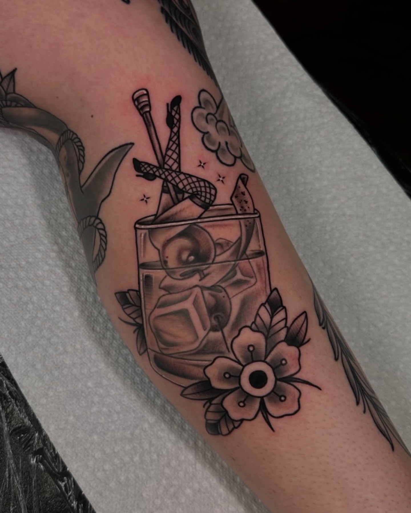 Whiskey glass with cocktail stick black and grey tattoo on the forearm by Teddi Garson