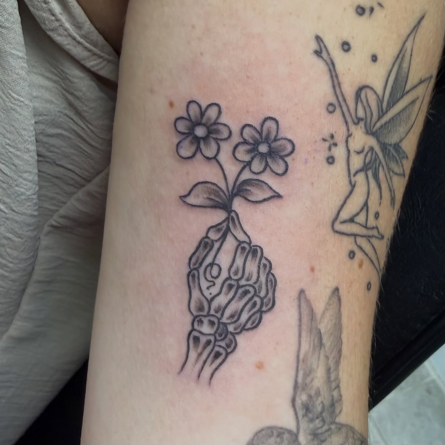 Flowers and skeleton hand black and grey tattoo on the forearm by Squid