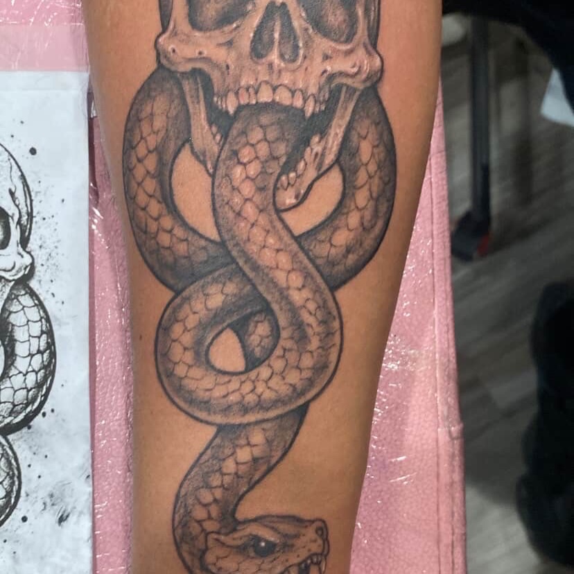 Snake and skull realism tattoo on the forearm by Hecho En El Bronx