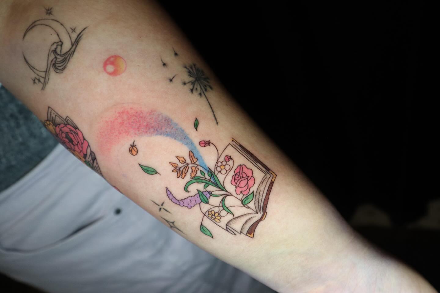 Book and flowers new school tattoo on the forearm by dani