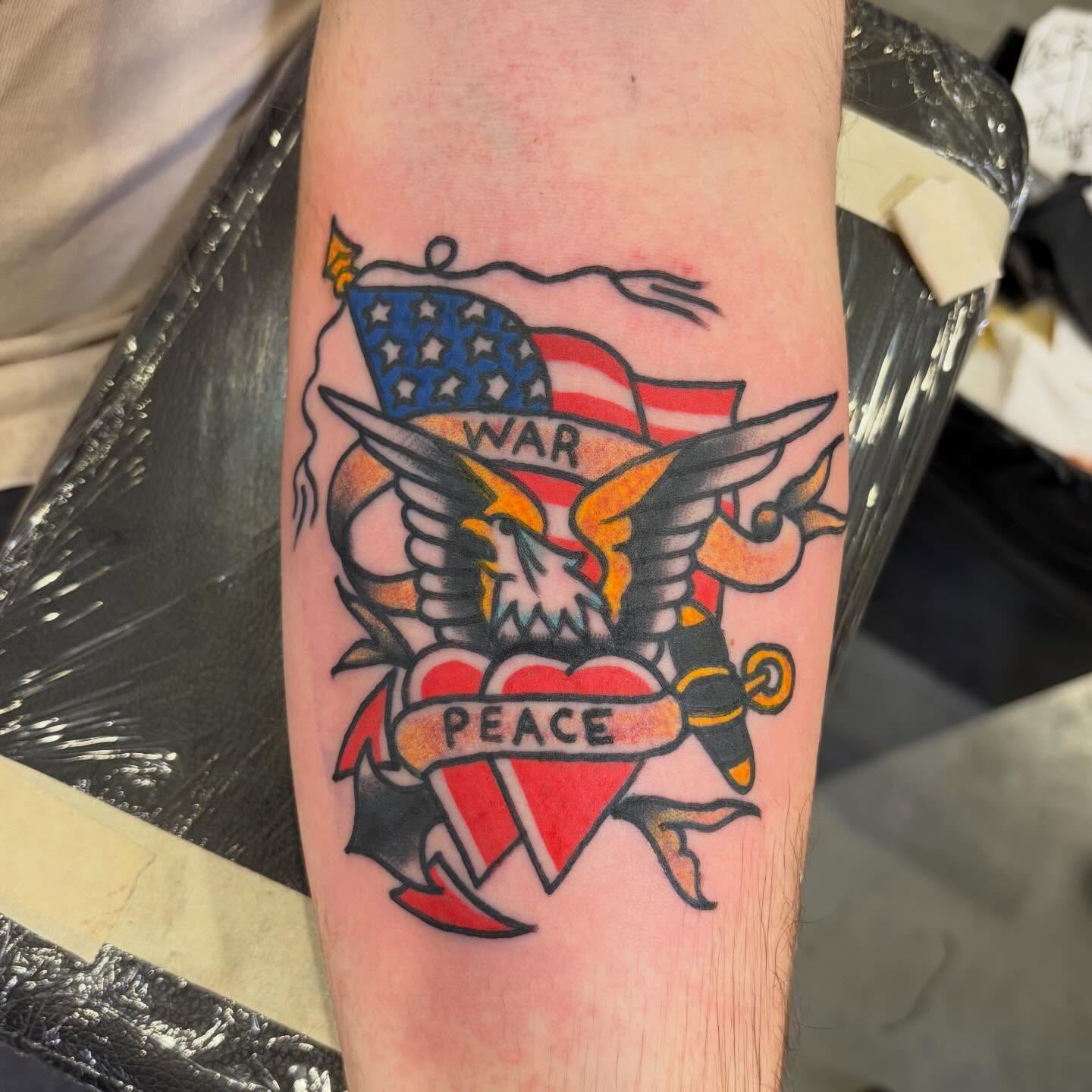 American flag, eagle, heart, peace/war American traditional tattoo on the forearm by Scrap Iron Tattoos