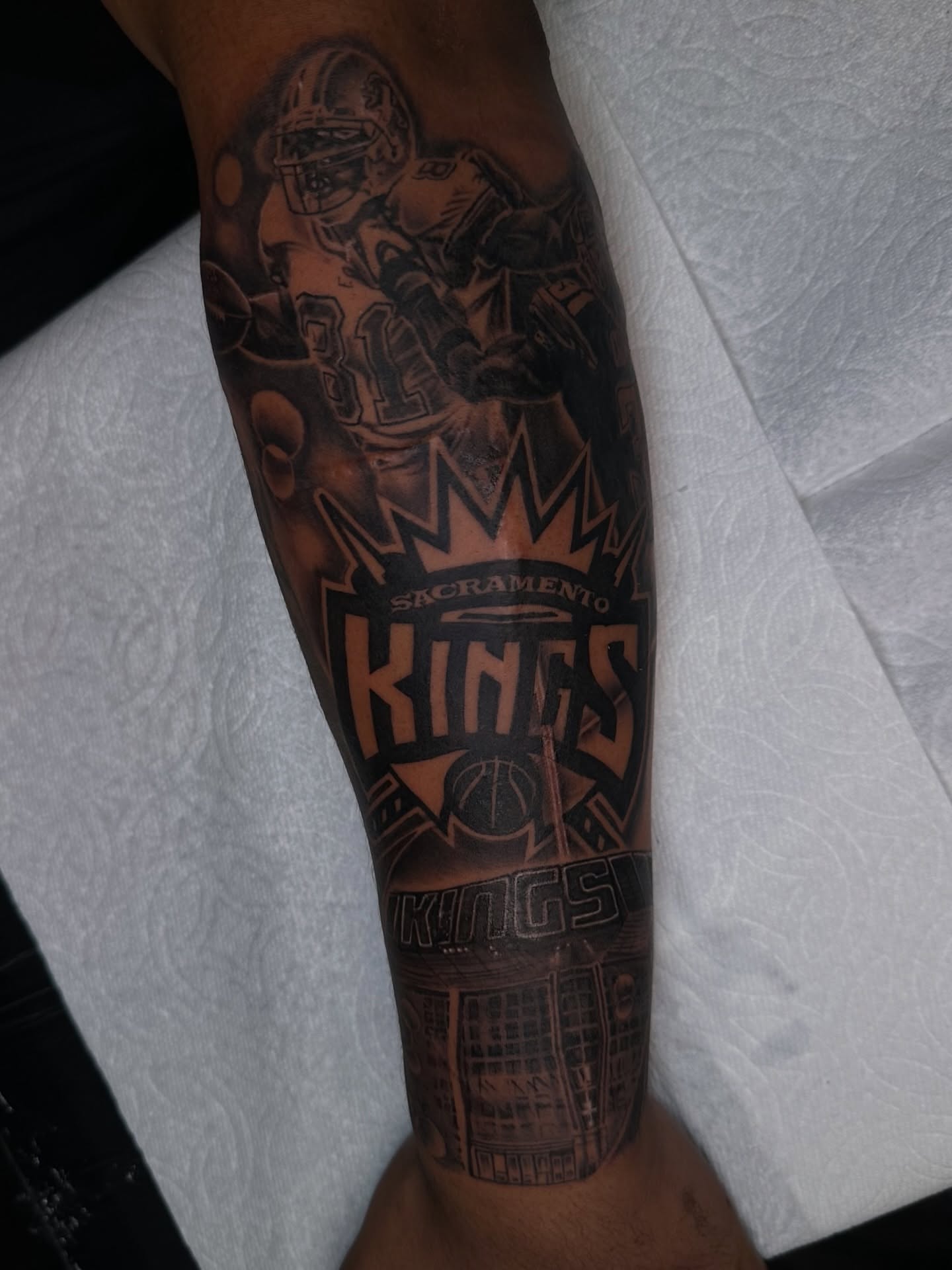 Basketball player and Sacramento Kings logo black and grey tattoo on the forearm by Mando