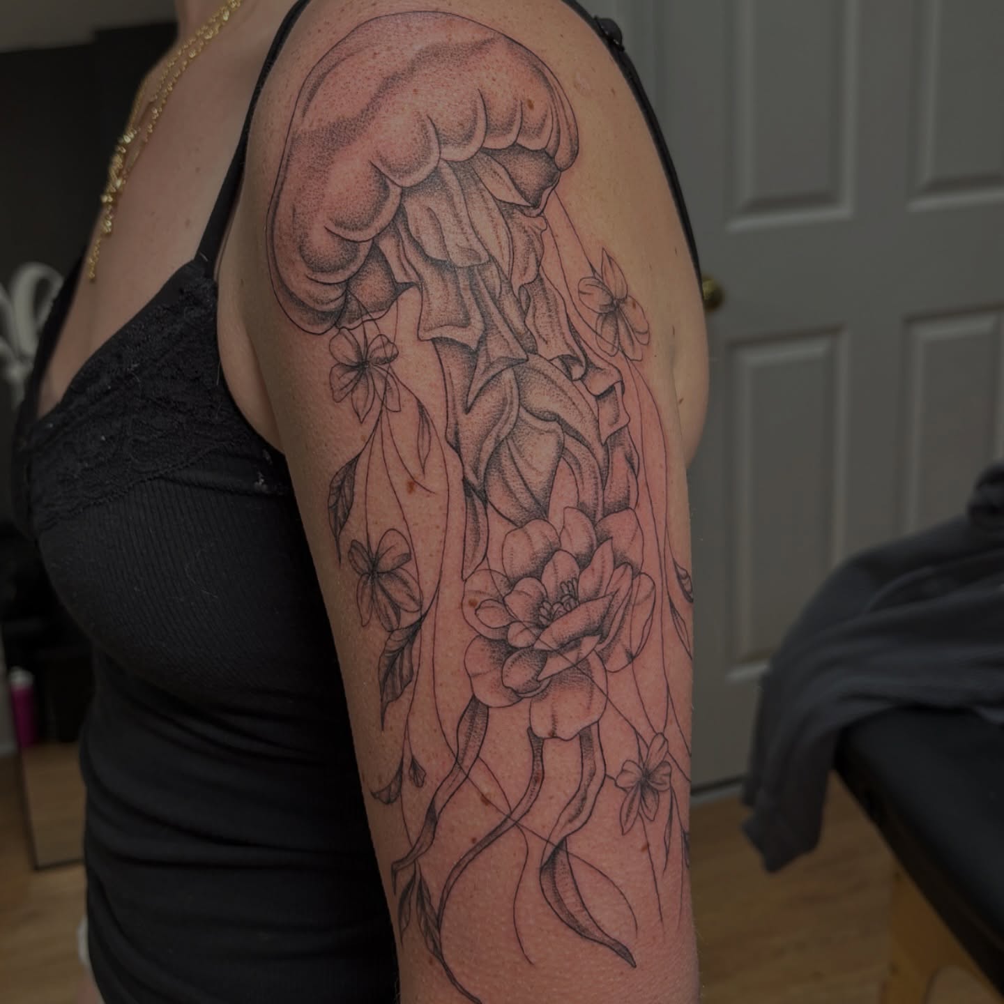 Jellyfish and flowers dotwork tattoo on the upper arm by Sydney Gallucci