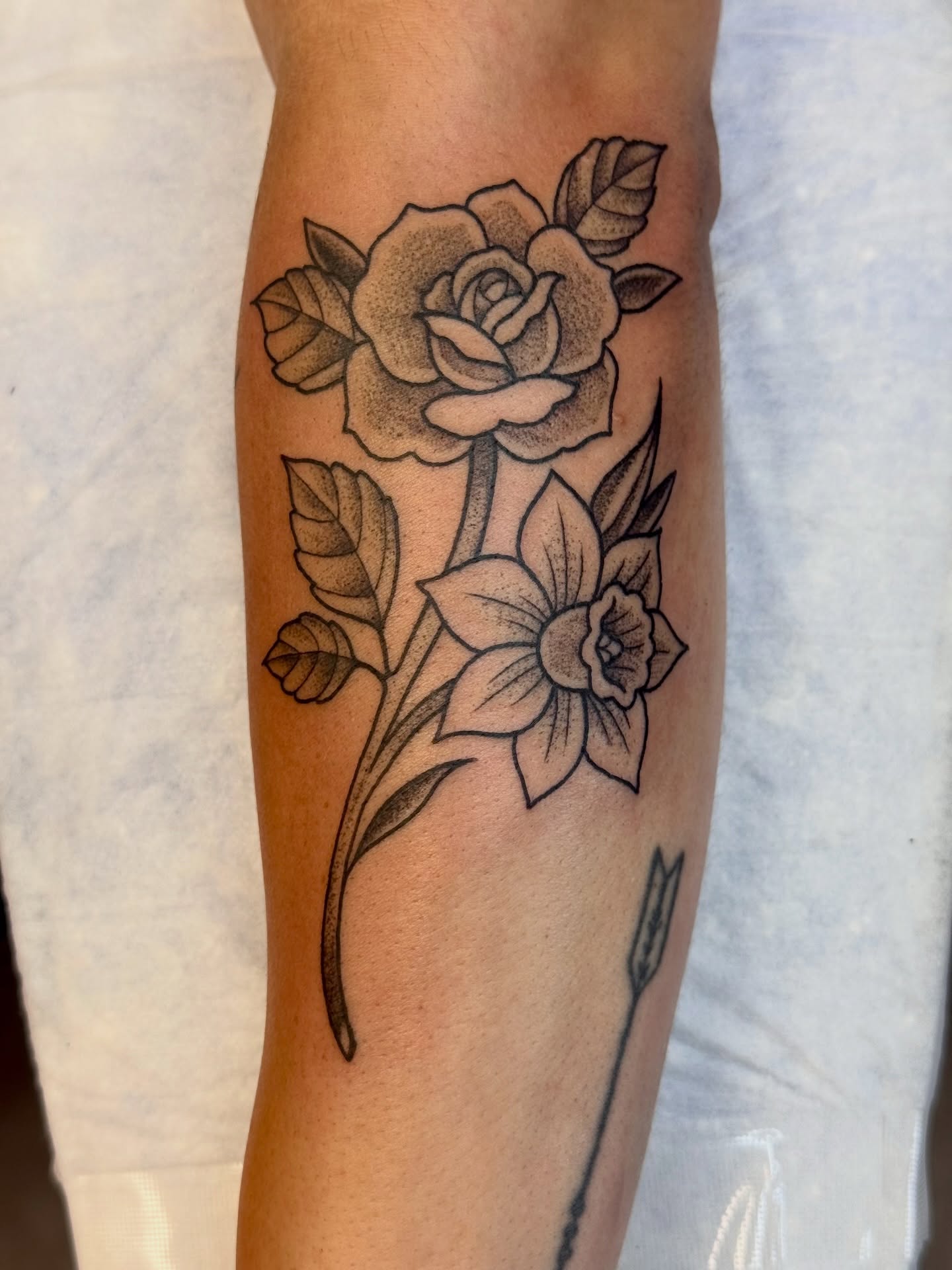 Rose and daffodil black and grey tattoo on the forearm by Caitlynn Austin