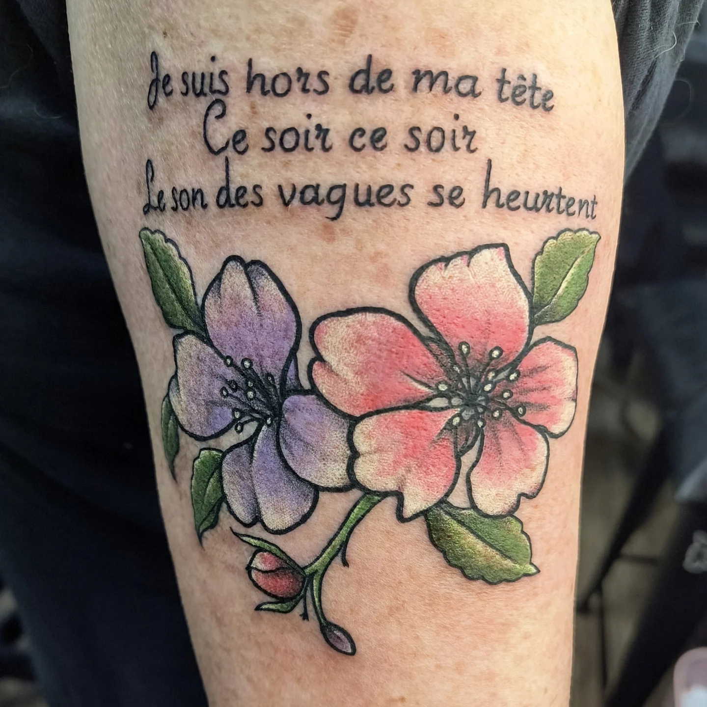 Flowers and French text watercolor tattoo on the forearm by Reid