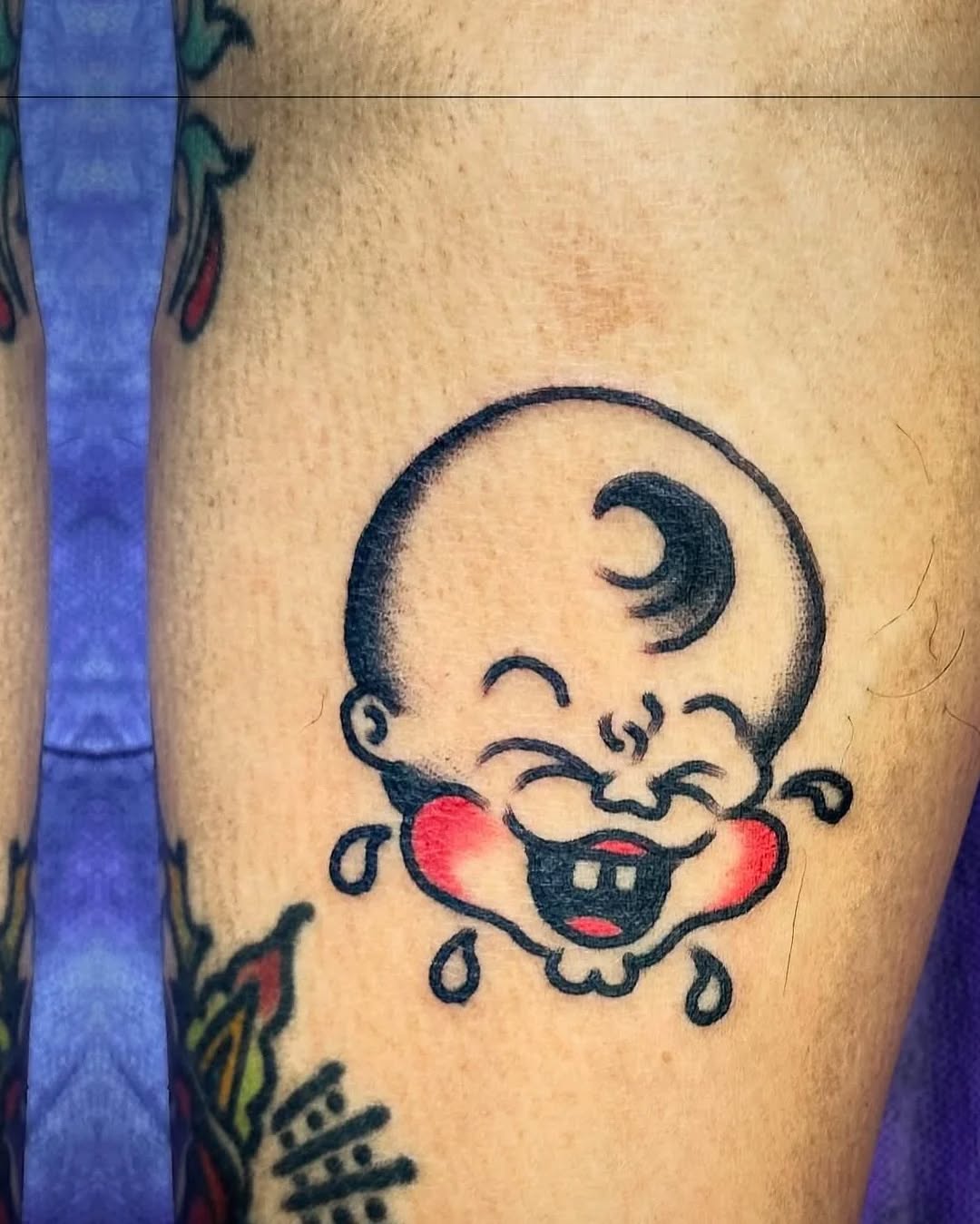 Laughing baby head new school tattoo on the thigh by Jaquelin Miller