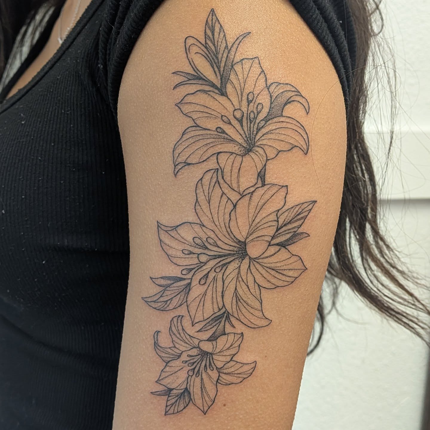 Lily black and grey tattoo on the upper arm by Ana Cielo Dueñas🌿Fernewt🌿Tattoo Artist🌿