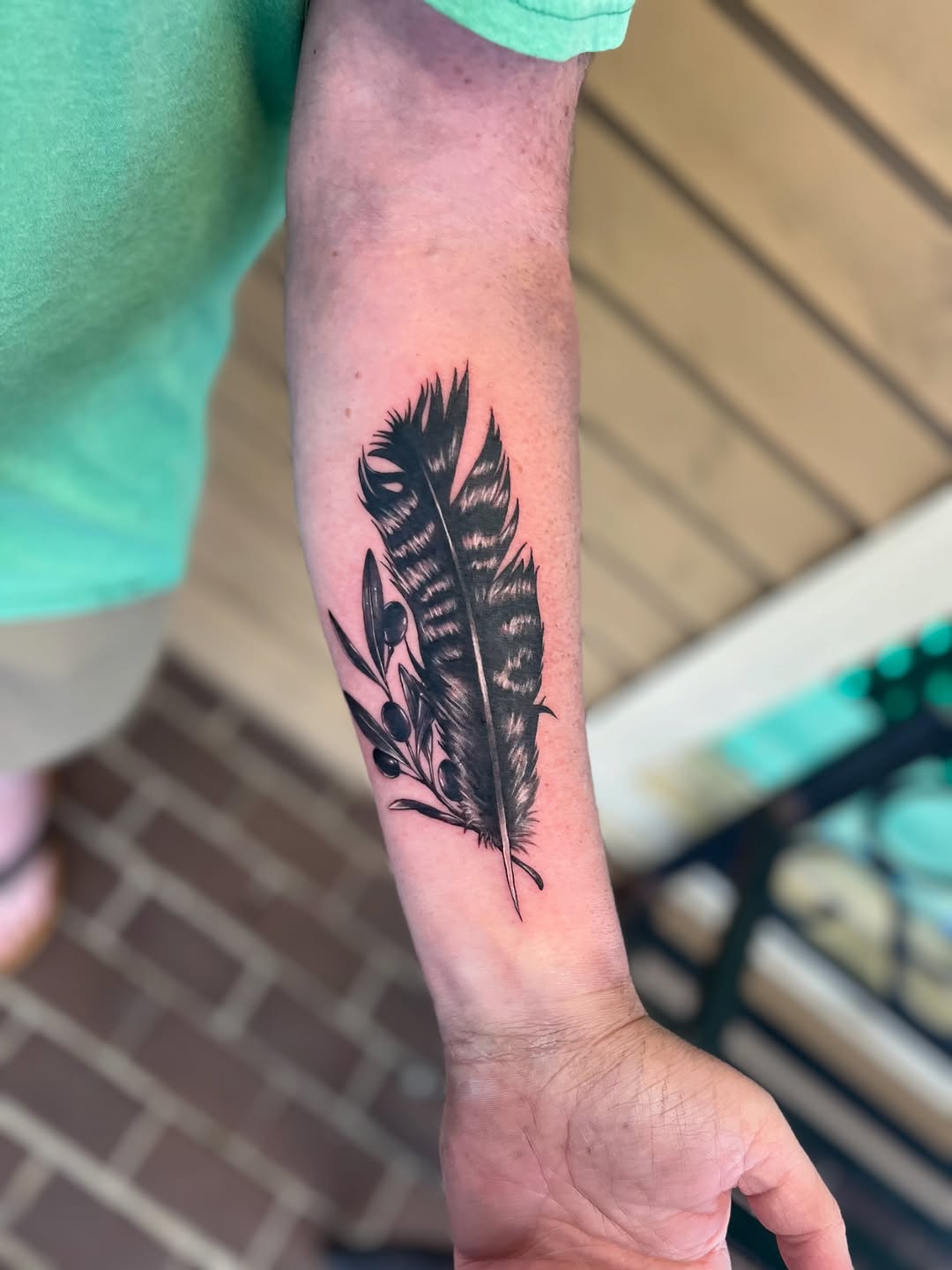 Feather and olive branch fine line tattoo on the forearm by Jai Woods
