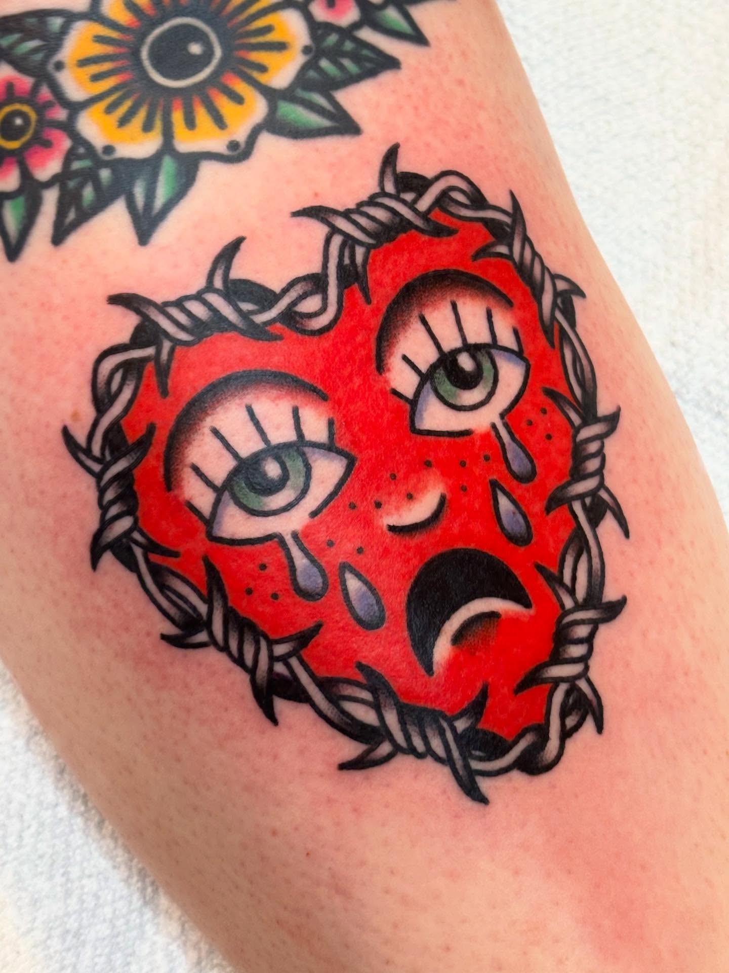 Red heart with eyes American traditional tattoo on the thigh by @rutattoos