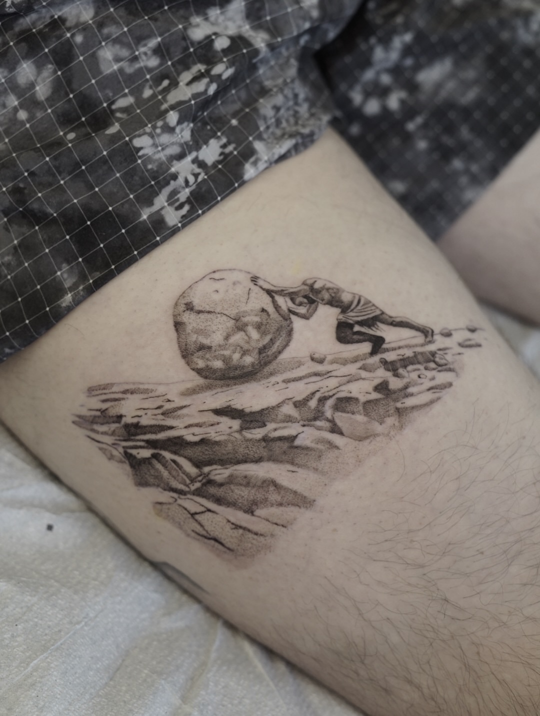 Man pushing rock black and grey tattoo on the thigh by Josh Infante