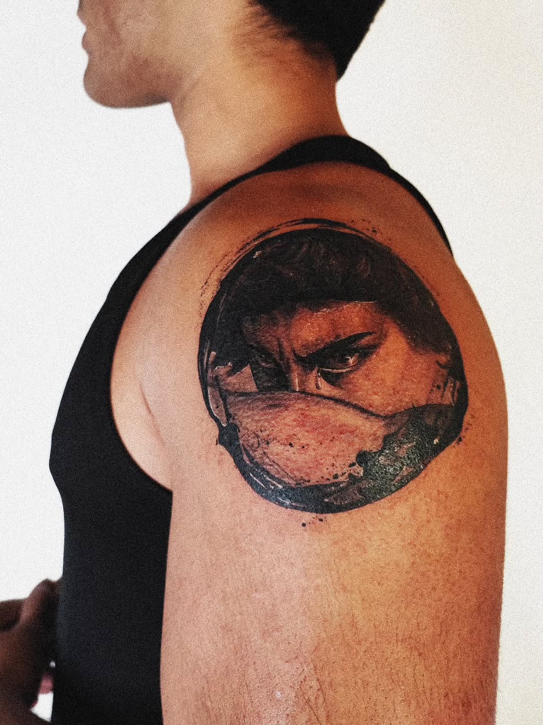 Mask-wearing figure realism tattoo on the shoulder by 𝗔𝗟𝗘𝗫 𝗣𝗥𝗘𝗤𝗨𝗘𝗟 𝗧𝗔𝗧𝗧𝗢𝗢𝗦 𝗖𝗛𝗜𝗖𝗔𝗚𝗢 ™, Chicago, Illinois